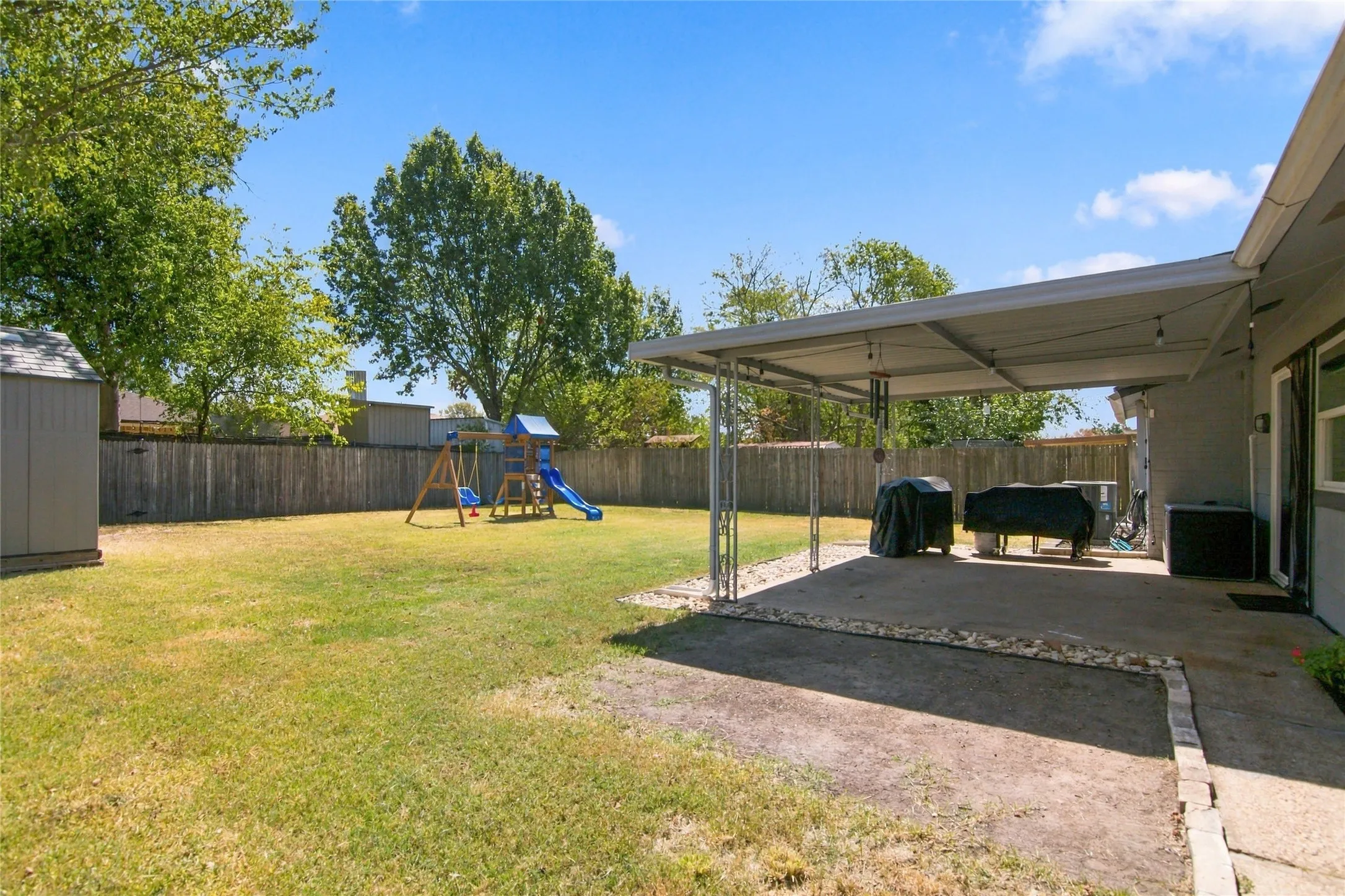 Expansive backyard featuring a covered patio, concrete paving, a wood privacy fence, and a storage shed