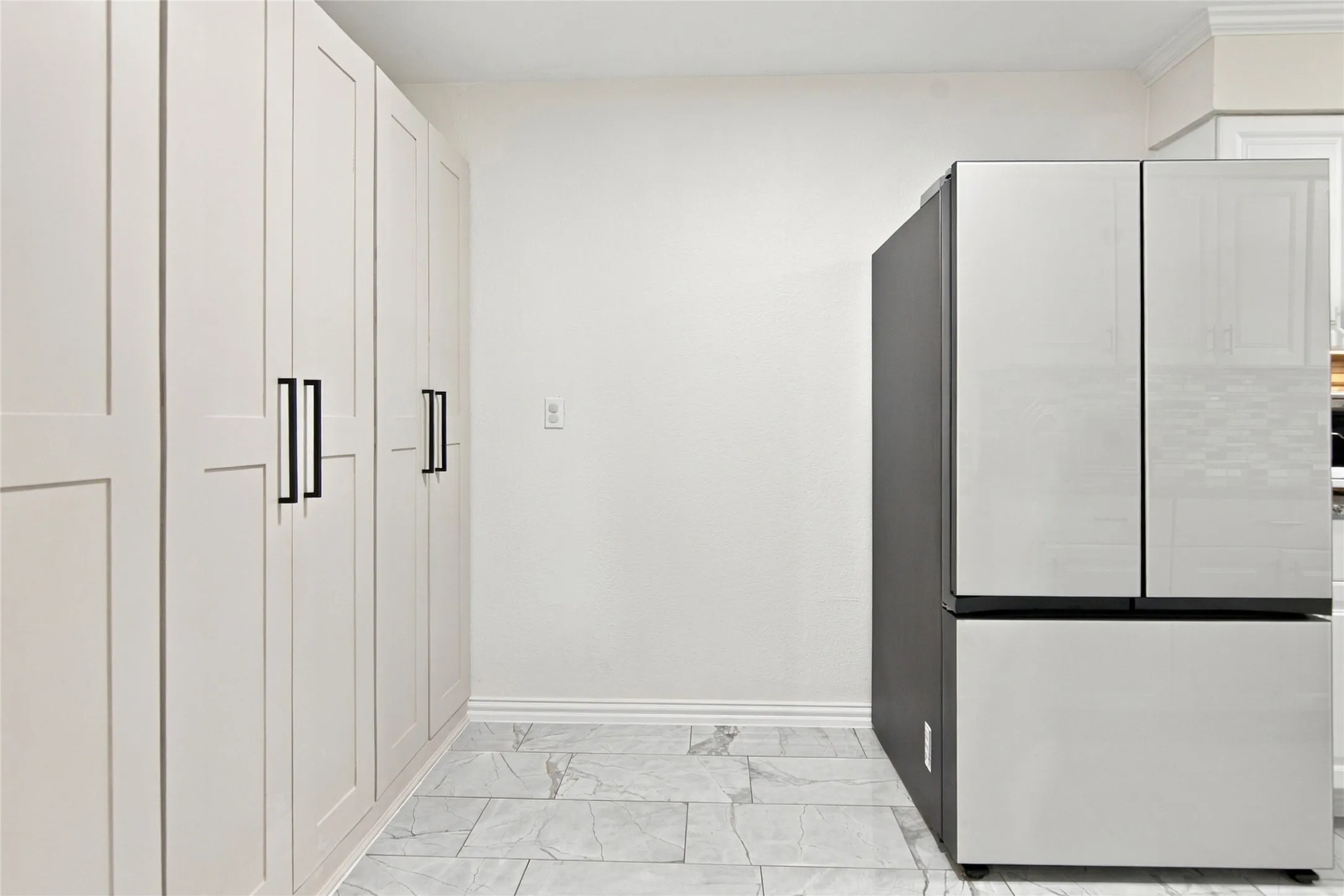Full-height cabinetry with matte black hardware, contemporary refrigerator with a black side panel, white walls, and light-toned tile flooring