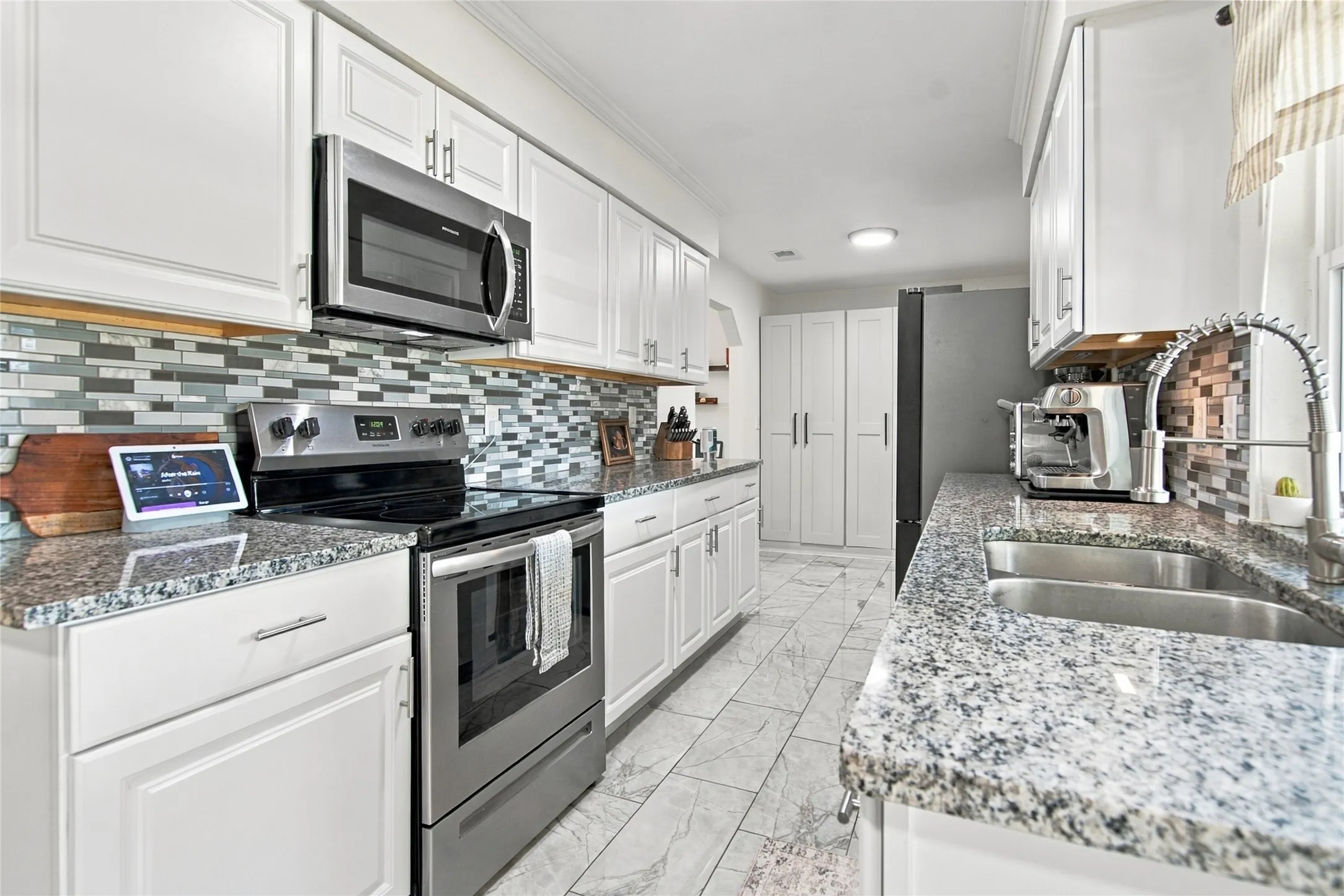 White cabinetry, stainless steel appliances, mosaic tile backsplash, double basin sink, and stone-finish countertops