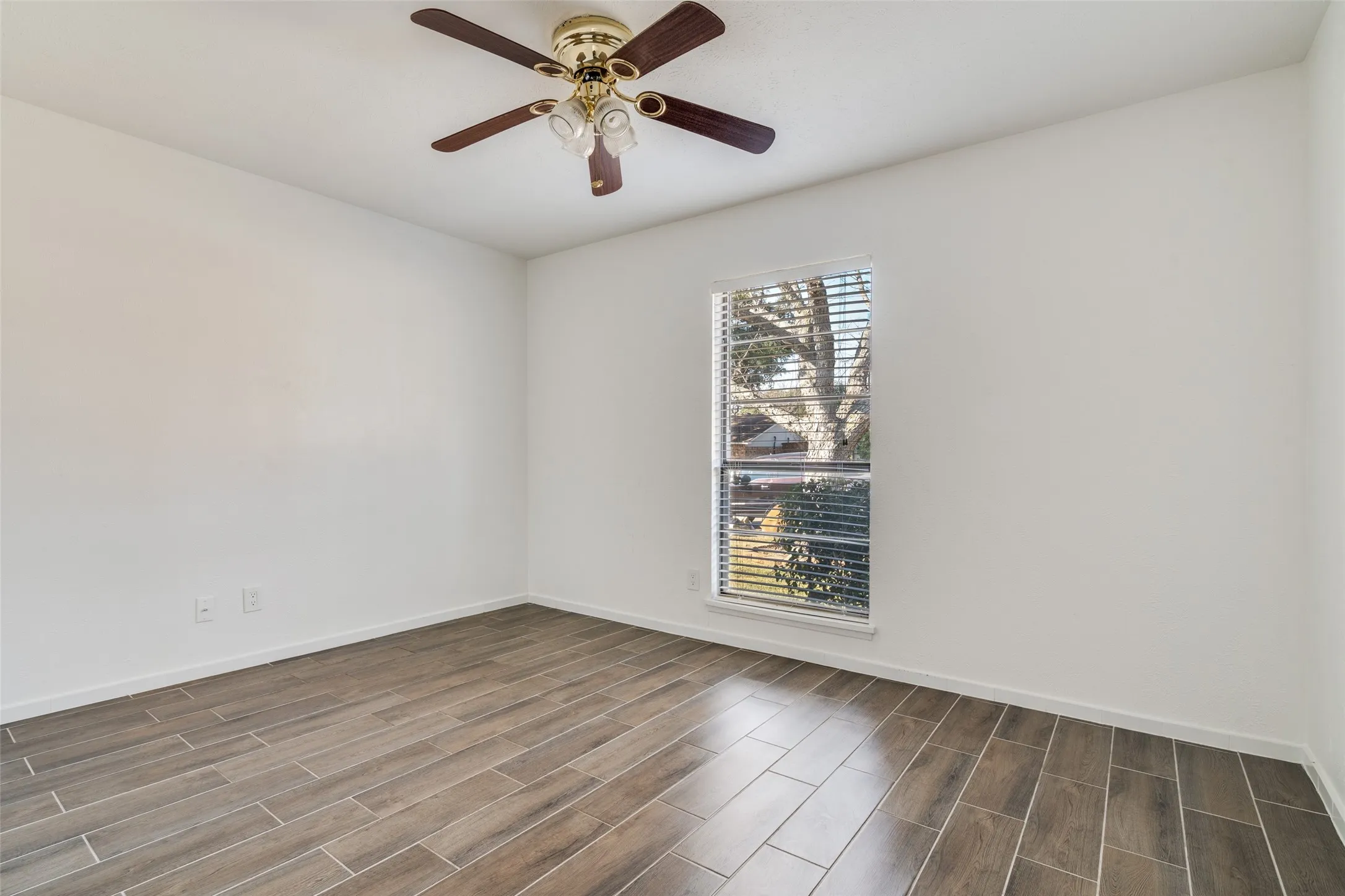 Wood-finish tile flooring throughout, featuring a ceiling fan with integrated lighting and a window with blinds