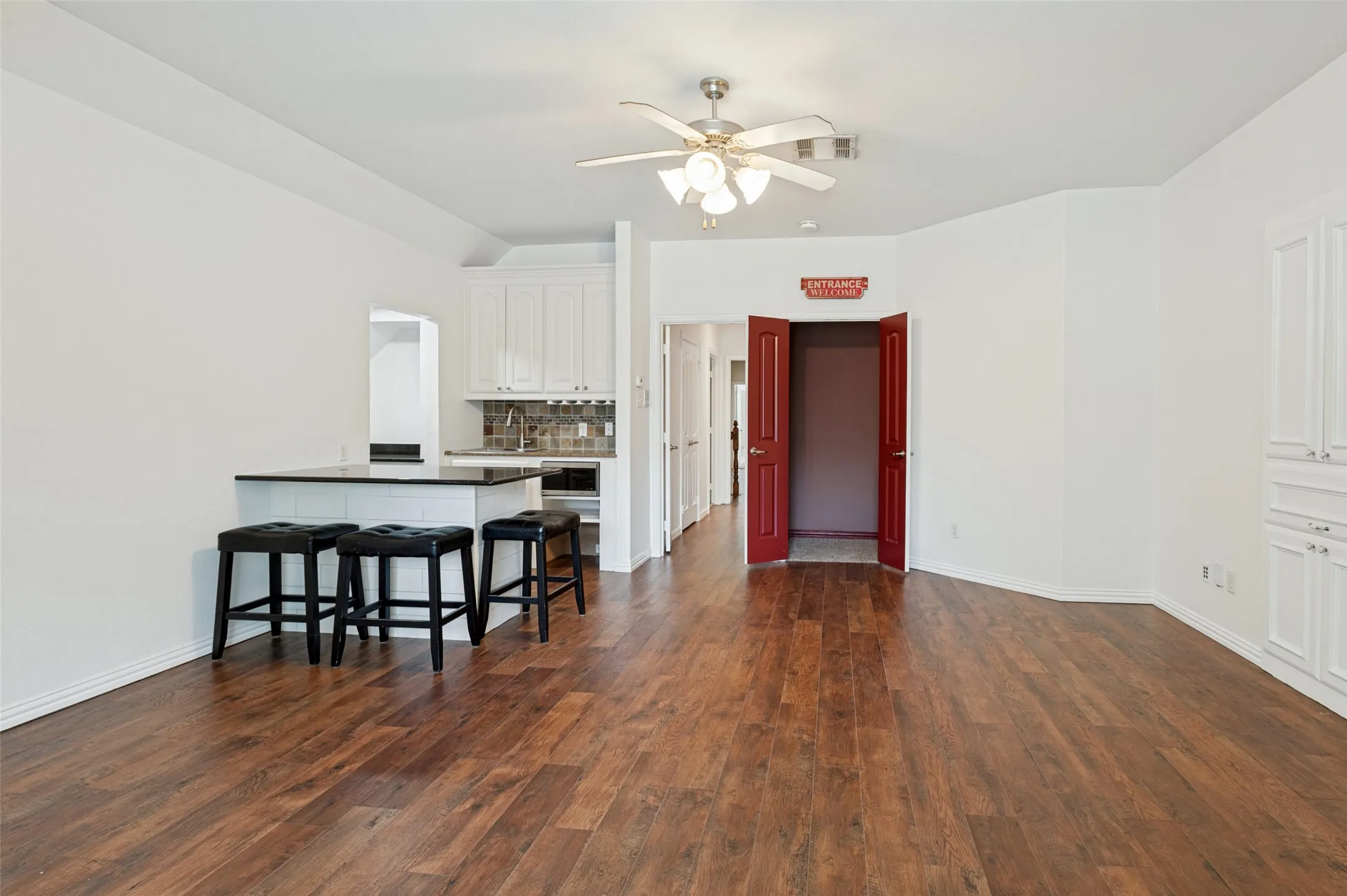 Wood-finish flooring, white cabinetry, island with countertop, ceiling fan, and built-in storage