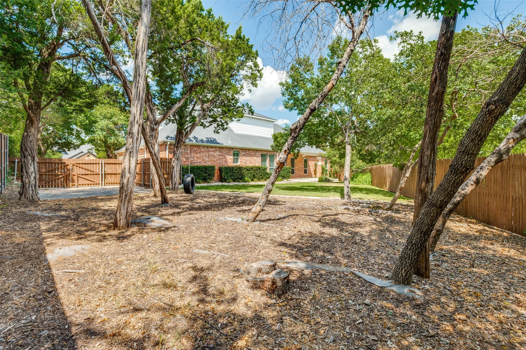 Expansive backyard with multiple mature trees, a wood privacy fence, and a brick exterior dwelling visible in the background