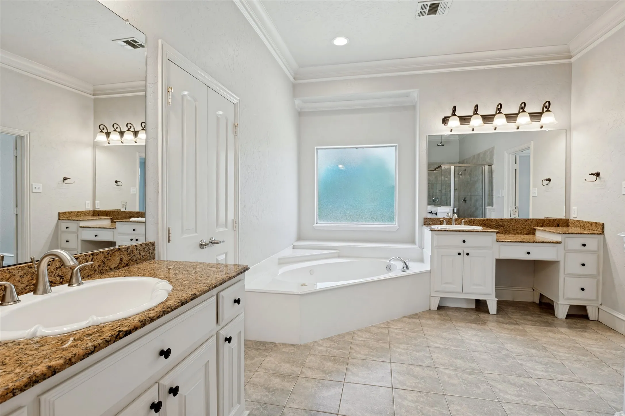Spacious bathroom featuring dual vanities with stone countertops, a built-in soaking tub, a large tiled shower, and tile flooring
