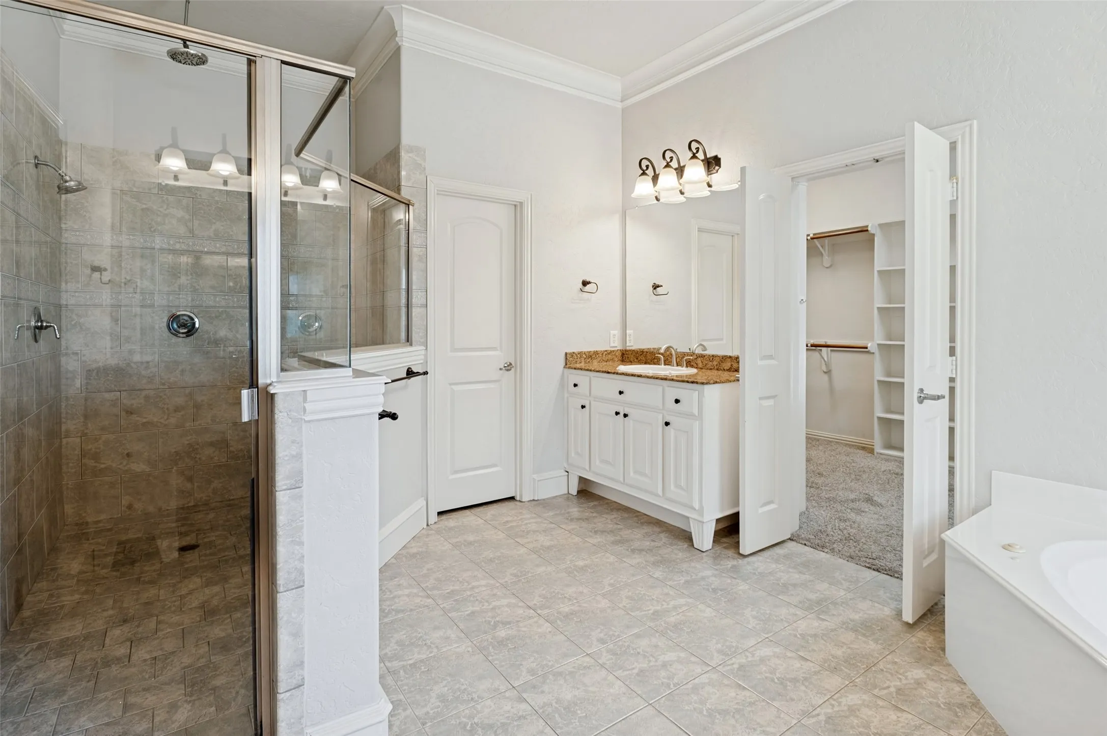 Glass-enclosed shower with tile surround, double vanity with stone countertop, tile flooring, and separate closet access