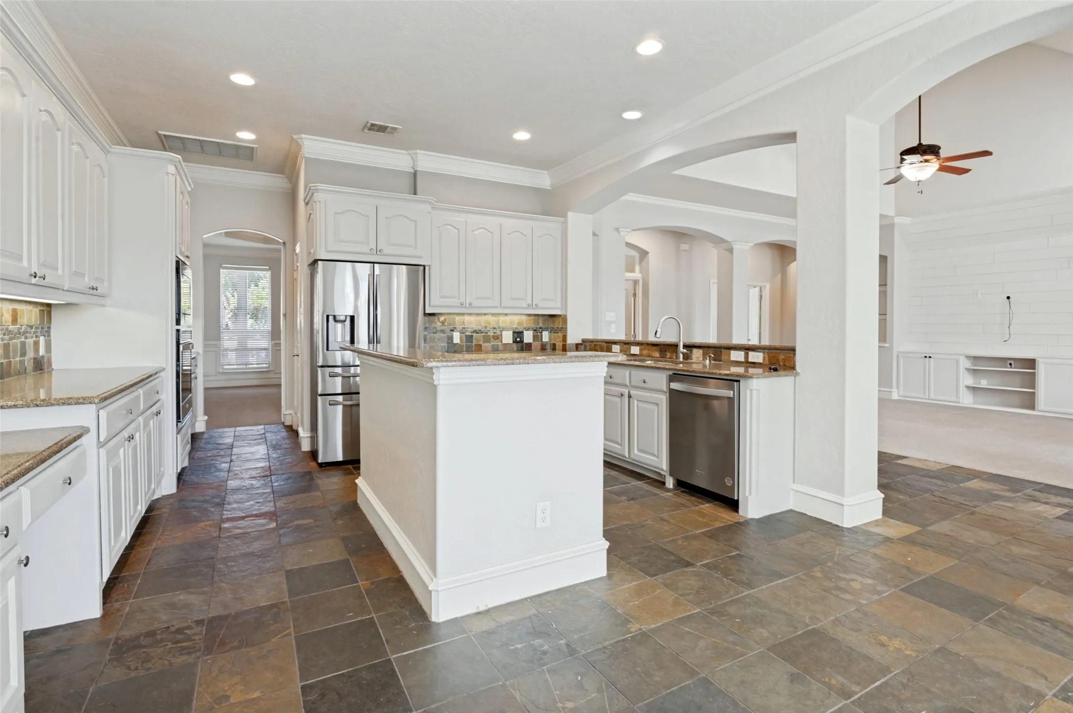 White cabinetry, stainless steel appliances, stone tile flooring, granite countertops, and recessed lighting
