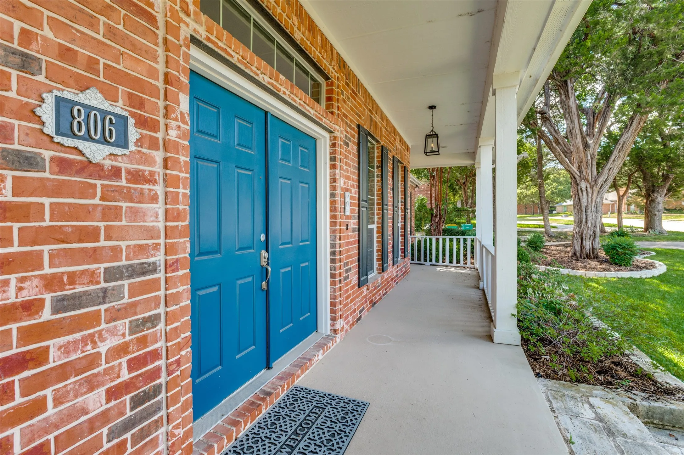 Brick exterior with a covered porch, blue double entry doors, transom window, and decorative house numbers