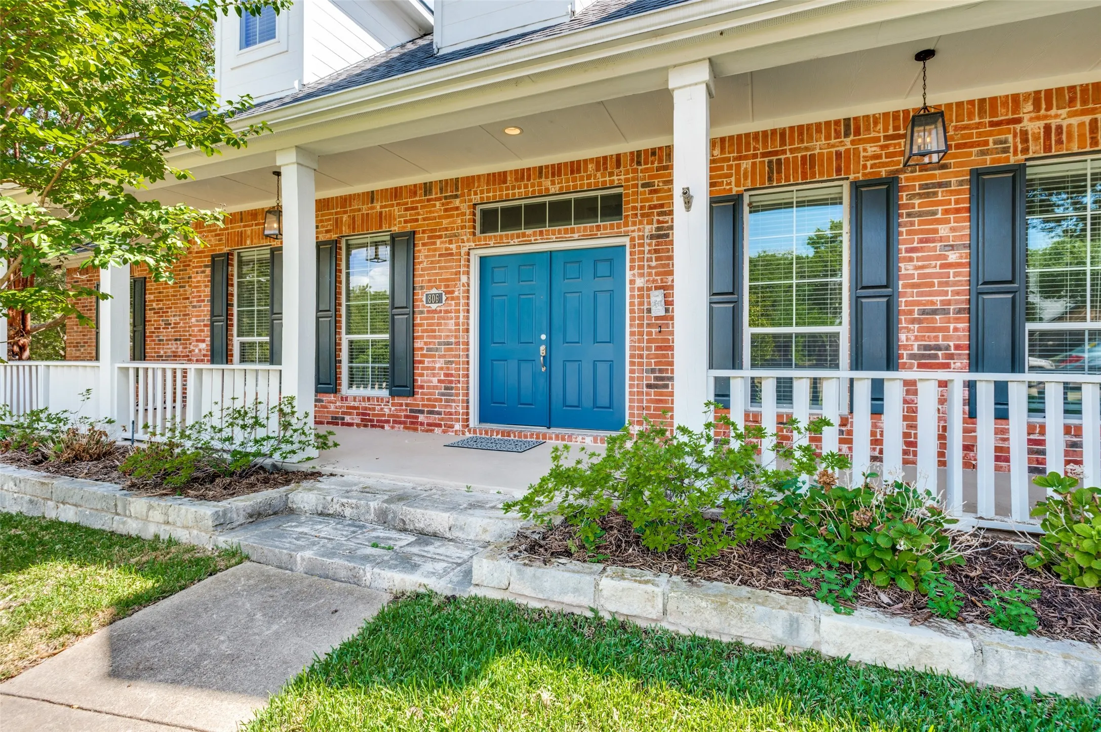 Brick exterior with a covered porch, white railing, and a vibrant blue double entry door
