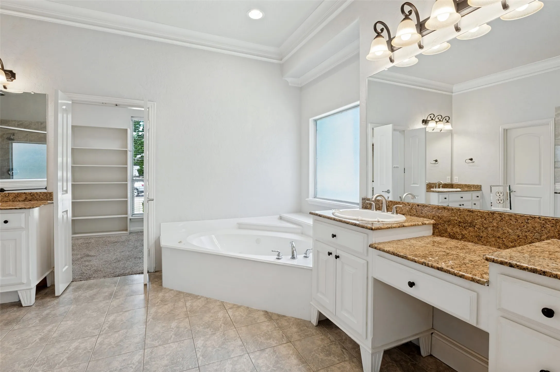 Bathroom featuring dual vanities with stone countertops, a built-in corner soaking tub, tile flooring, and crown molding