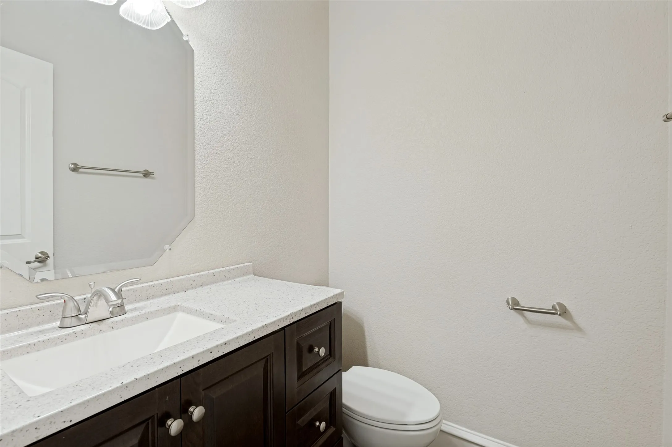 Dark wood-finish vanity with an integrated sink, light-toned countertop, brushed nickel faucet, and an octagonal mirror