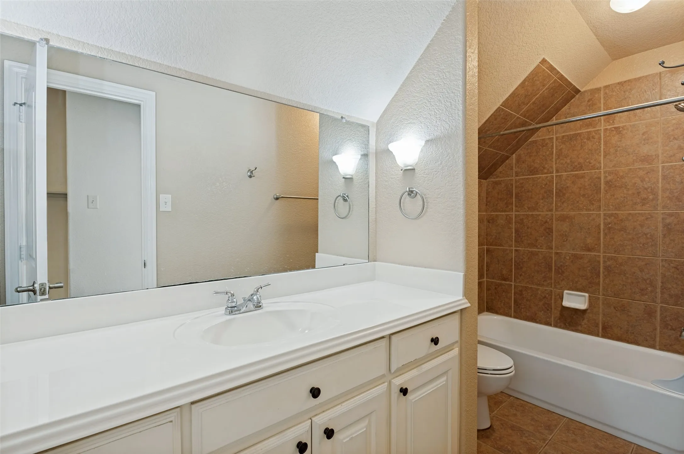 White vanity with integrated sink, chrome faucet, wall-mounted sconces, and a large mirror