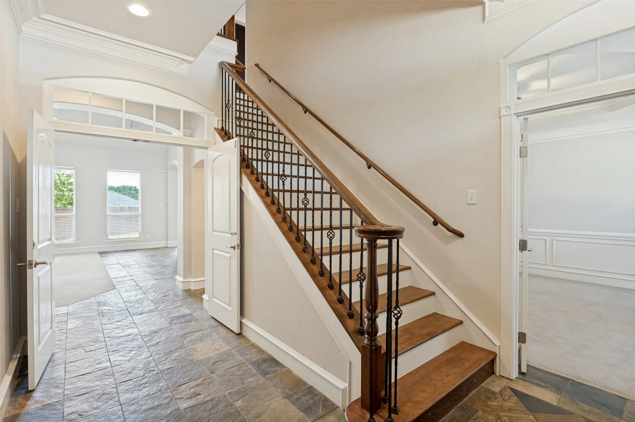 Slate tile flooring, hardwood staircase with wrought iron balusters, arched entryway with transom window, and recessed lighting