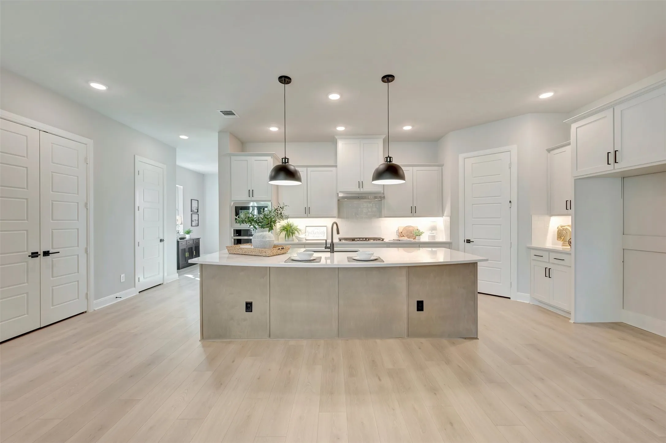 Kitchen featuring a light-toned wood-finish floor, recessed lighting, white cabinetry, a large central island with a light-toned countertop, and two pendant lights