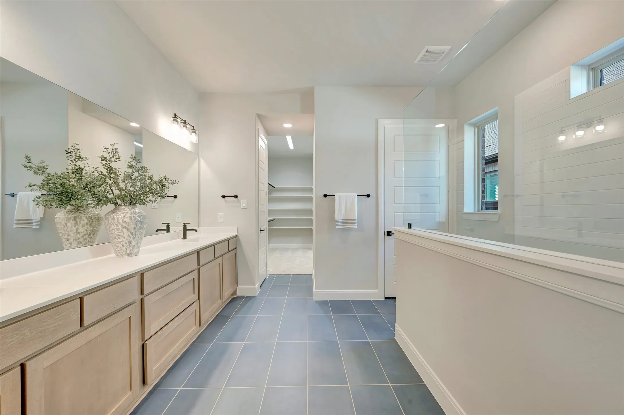 Dual vanity with light wood-finish cabinetry, a large integrated mirror, and matte black fixtures