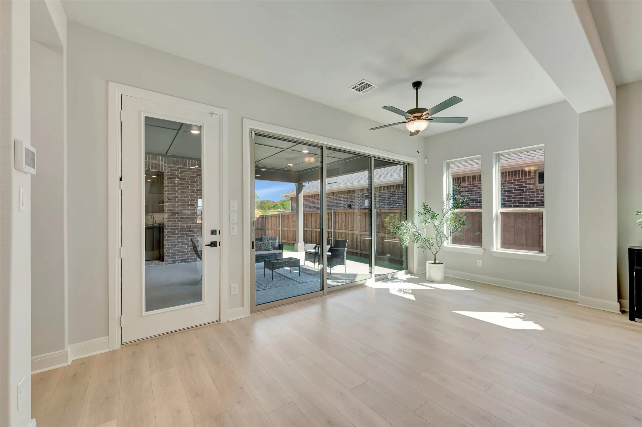 Light wood-finish flooring, ceiling fan with integrated lighting, glass-paneled patio door, large sliding glass doors, and multiple windows