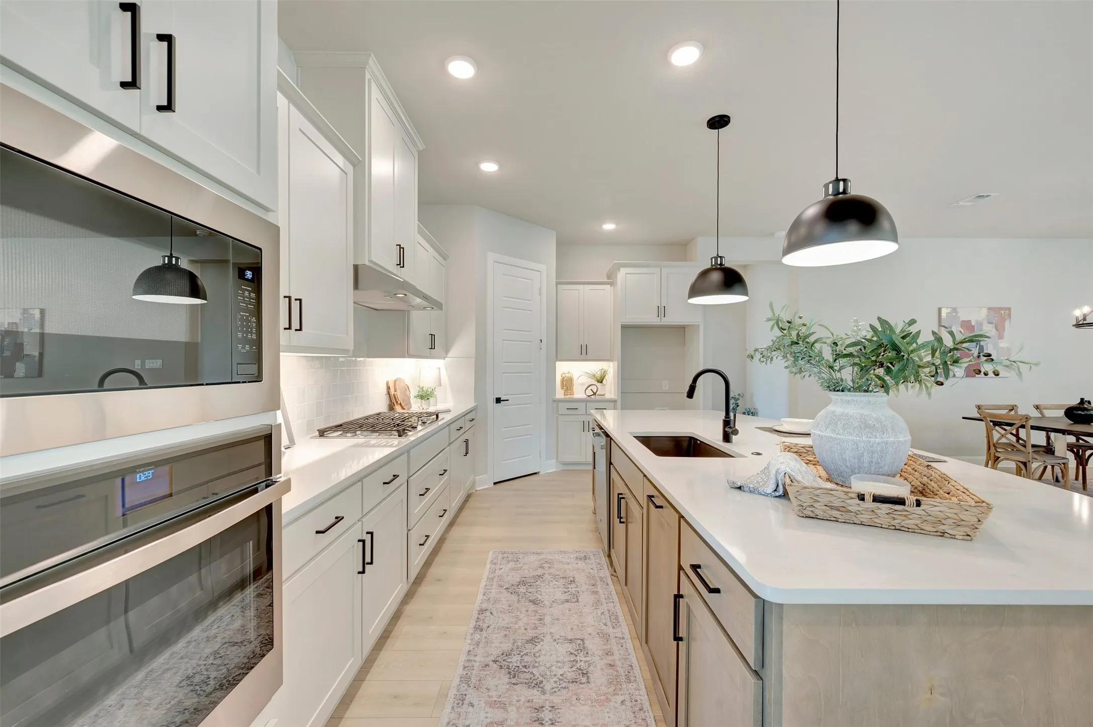 Gourmet kitchen with stainless steel appliances, white shaker cabinetry, an expansive island with a sink, pendant lighting, and wood-finish flooring