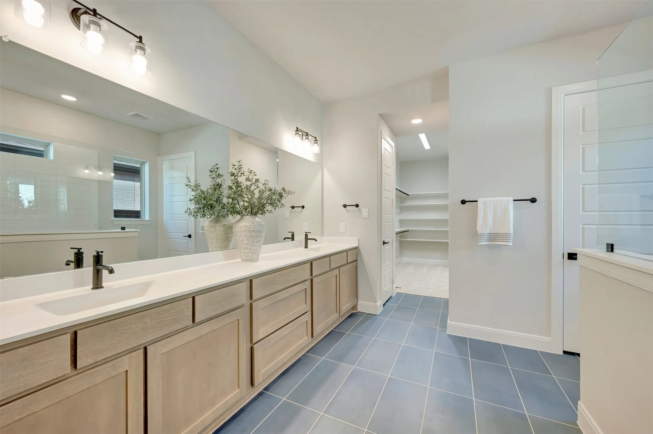 Dual vanity with integrated sinks, expansive mirror, wood-finish cabinetry, and blue tile flooring