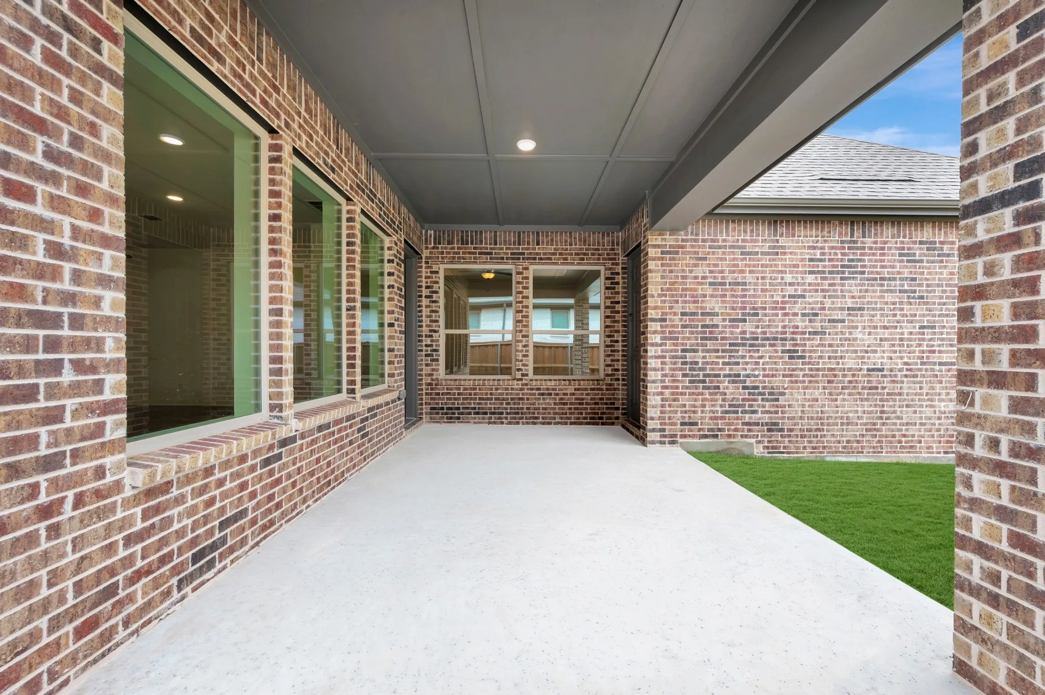 Covered patio with a concrete surface, brick exterior, multiple windows, recessed lighting, and a manicured lawn
