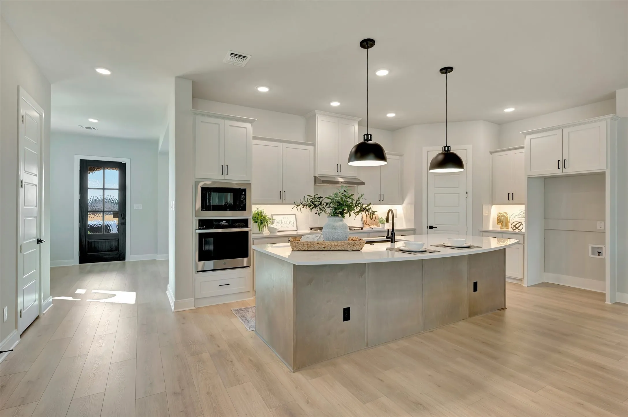 Modern kitchen featuring white cabinetry, a spacious island with pendant lighting, integrated stainless steel appliances, and wood-finish flooring