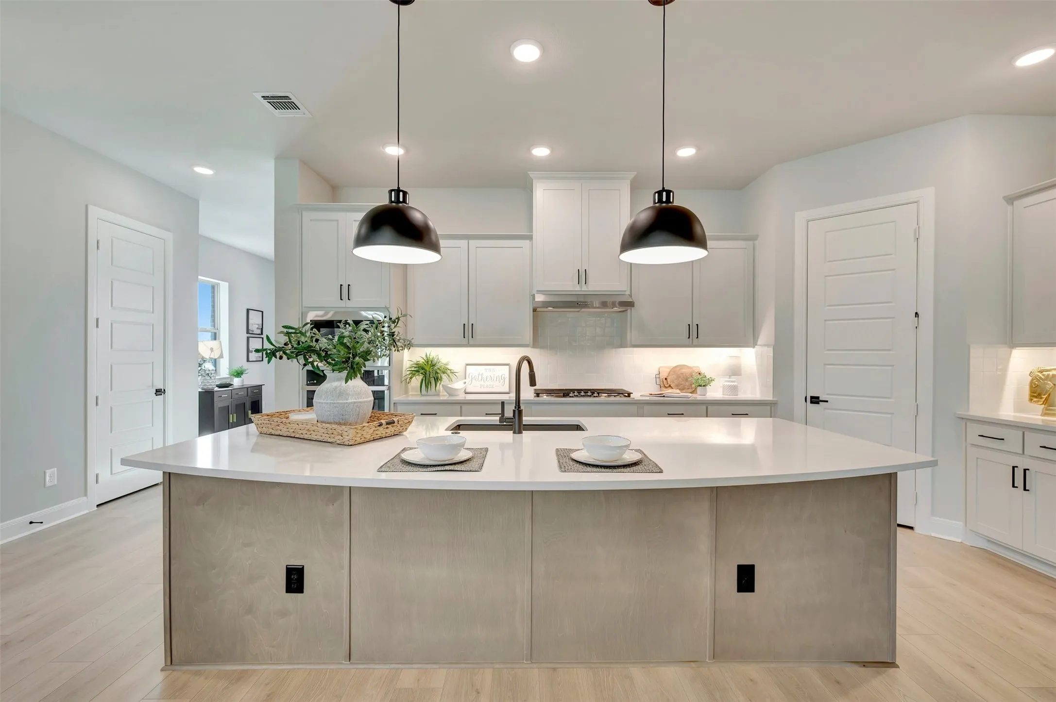 Kitchen featuring a curved central island with a light-toned base, light countertops, and two matte black pendant lights