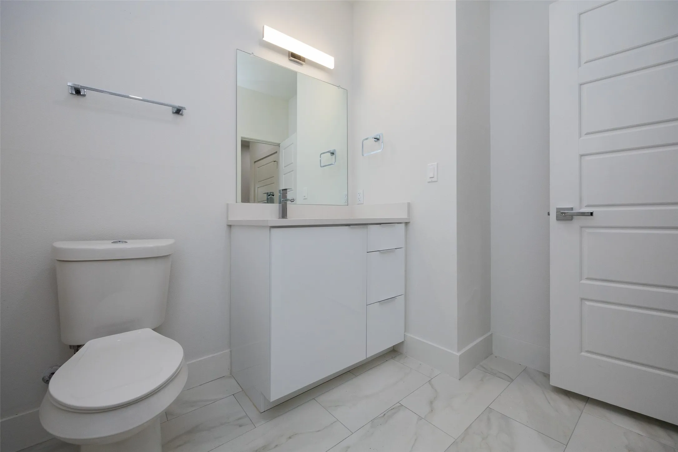 White vanity with integrated sink, modern lighting fixture, panel door, chrome hardware, and tile flooring