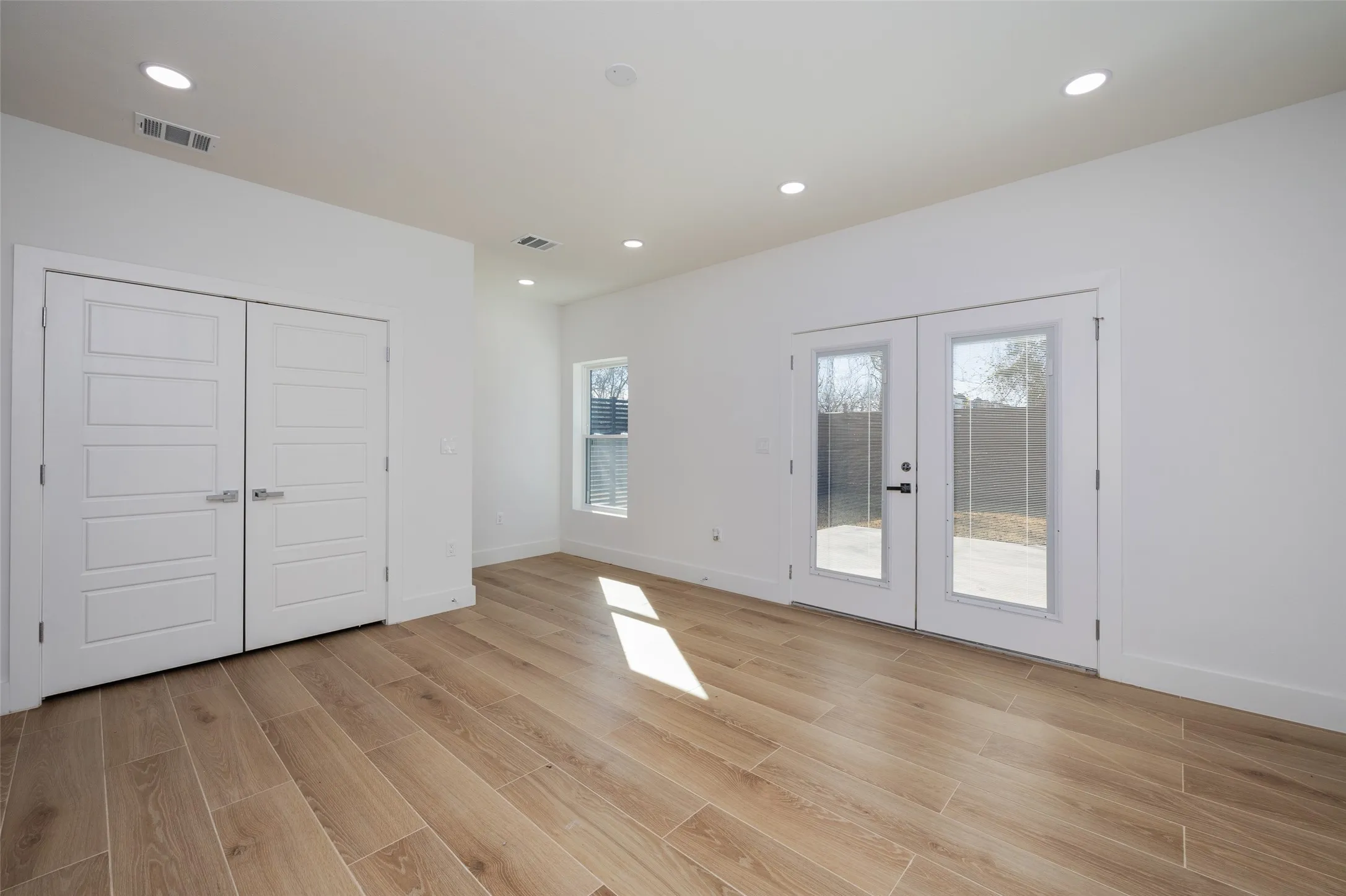 Recessed lighting, wood-finish flooring, white walls, and double French doors opening to an outdoor patio