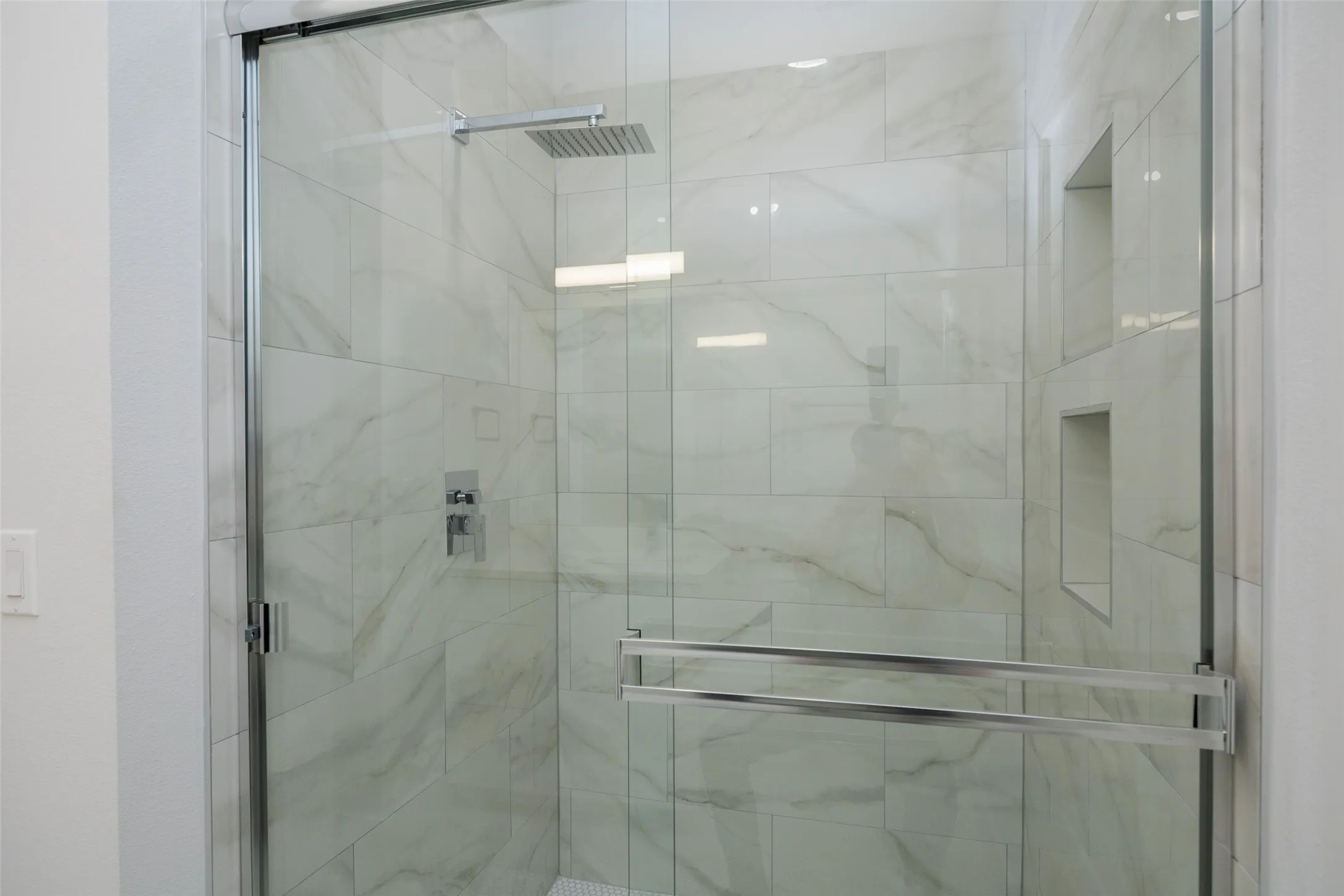 Glass-enclosed shower with a rainfall showerhead, polished chrome fixtures, and integrated wall niches