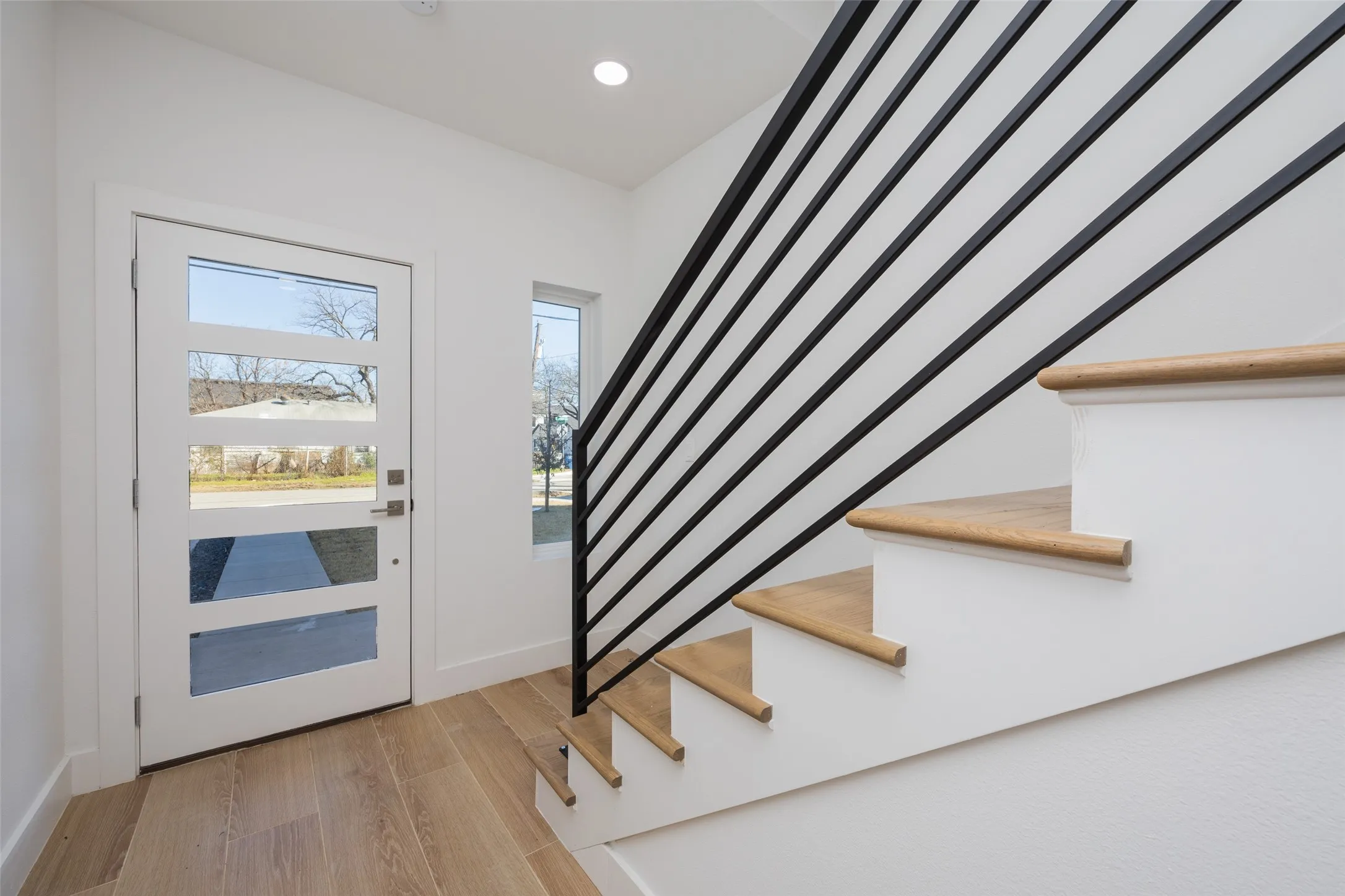 White entry door with frosted glass panels, wood-finish flooring, and a staircase featuring a black metal railing and wood treads