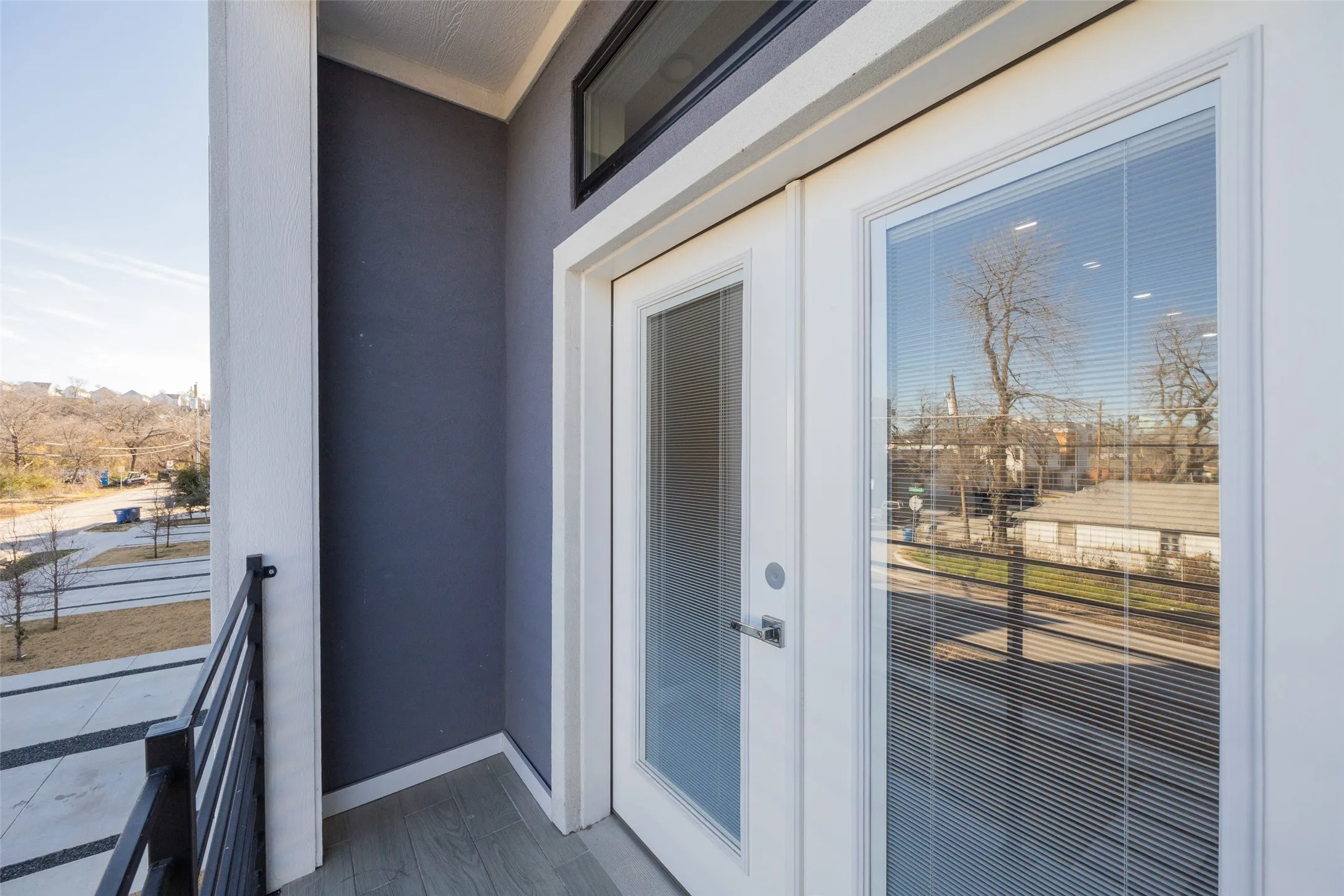 Balcony featuring wood-look flooring, a wrought iron railing, and a white double door with integrated blinds