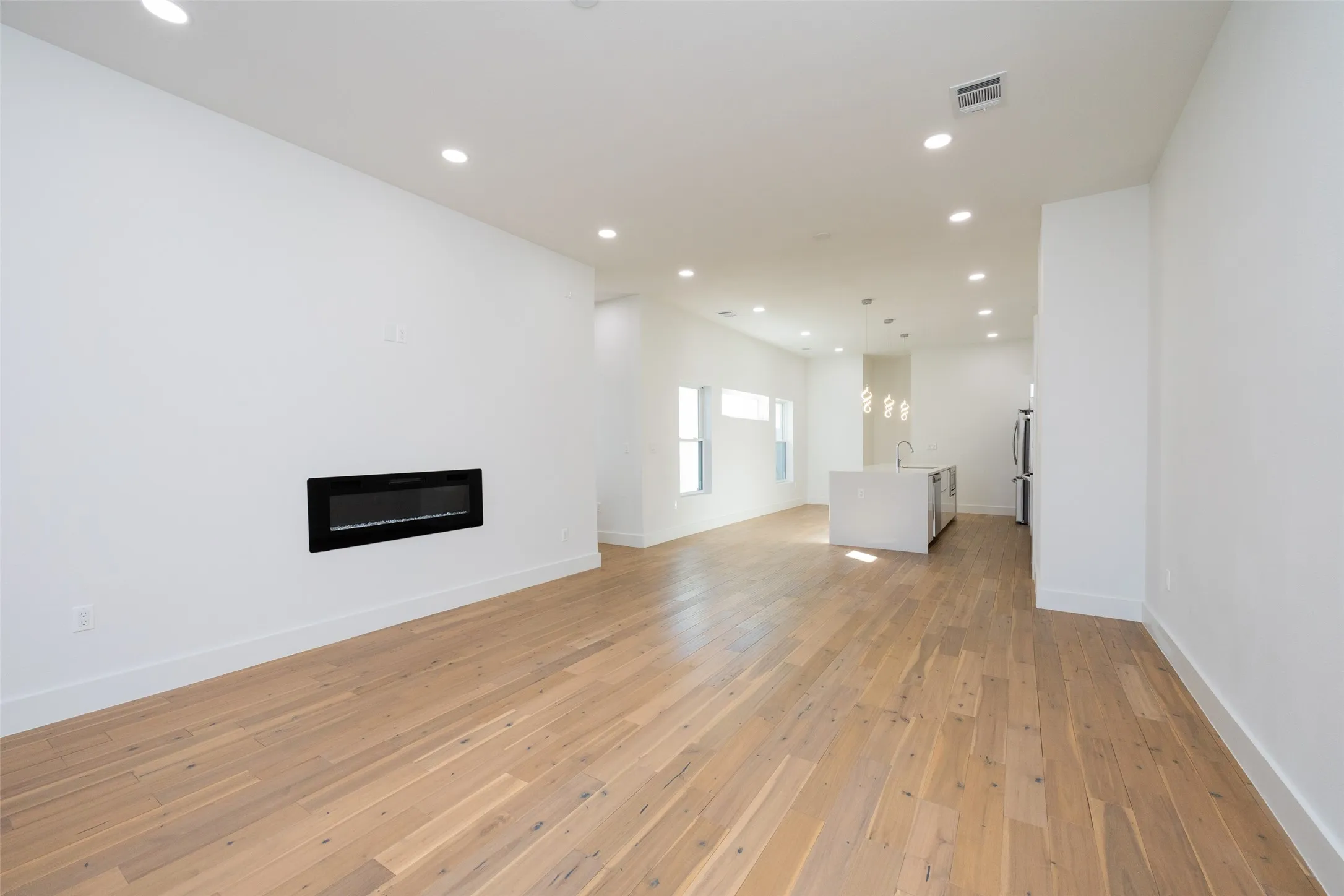 Bright open-concept living space showcasing warm wood-finish flooring throughout, recessed ceiling lighting, and clean white walls