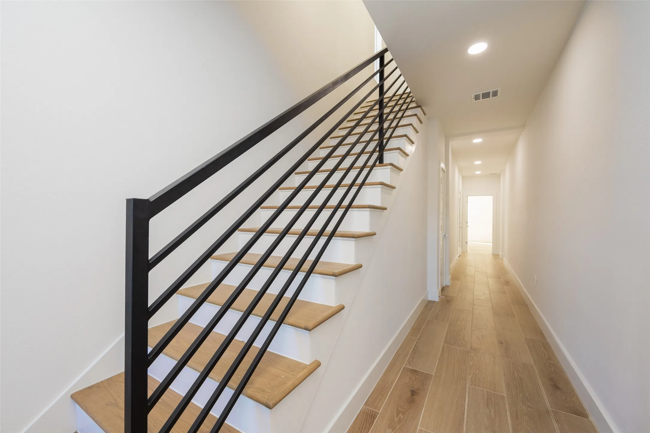 Staircase featuring wood-finish treads and risers, black metal railing, and recessed lighting