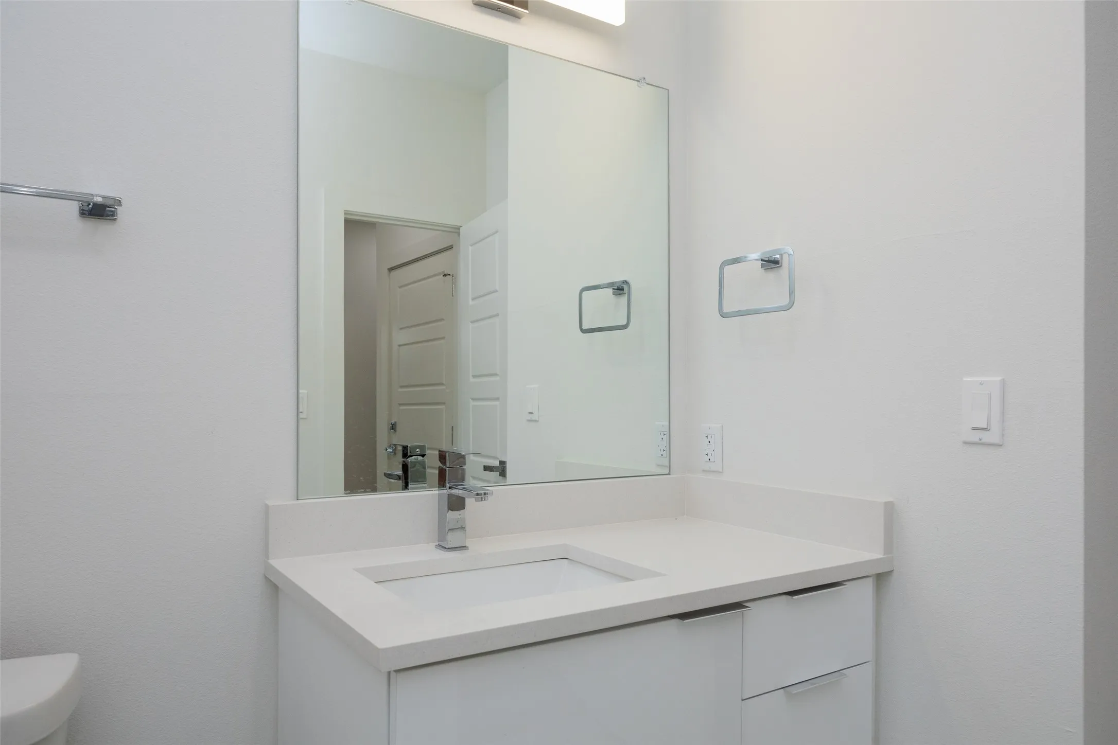 White vanity with an integrated rectangular sink, chrome faucet, and expansive wall-mounted mirror