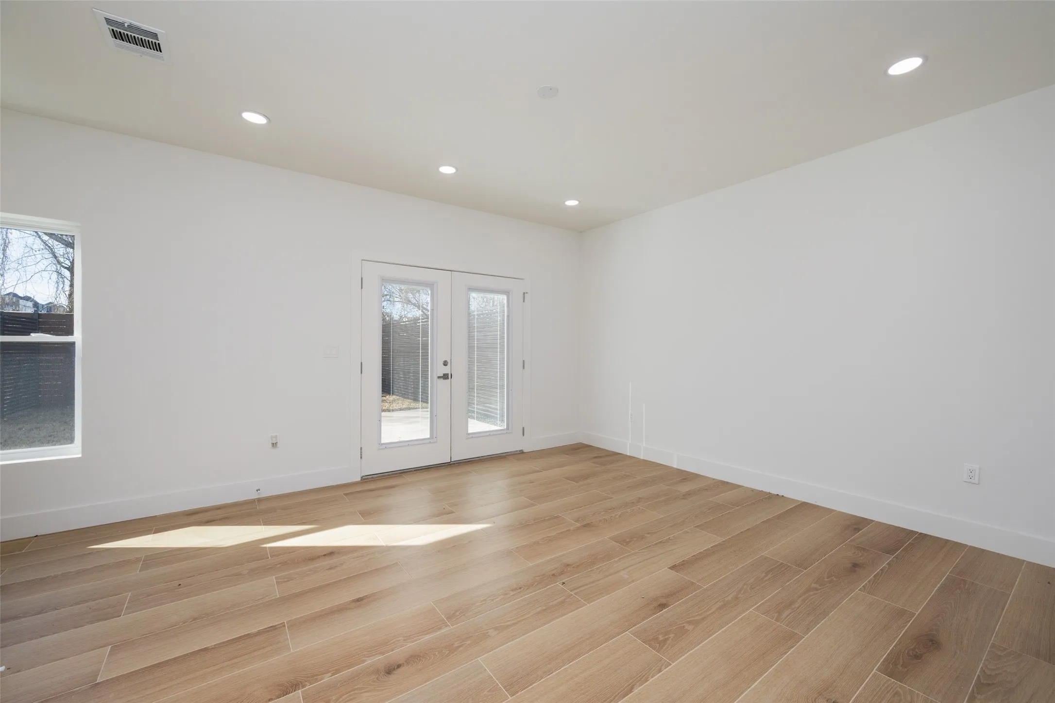 Recessed ceiling lighting, wood-finish flooring, white walls, and double glass-paneled doors