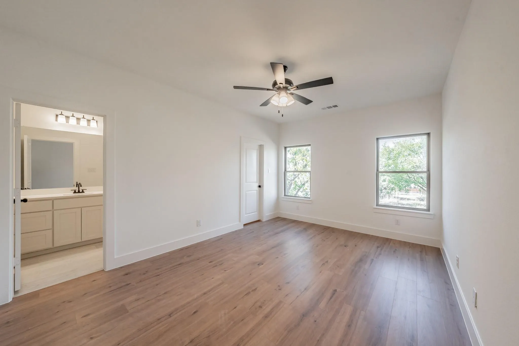 Spacious room with wood-finish flooring, two windows, and a ceiling fan with integrated lighting