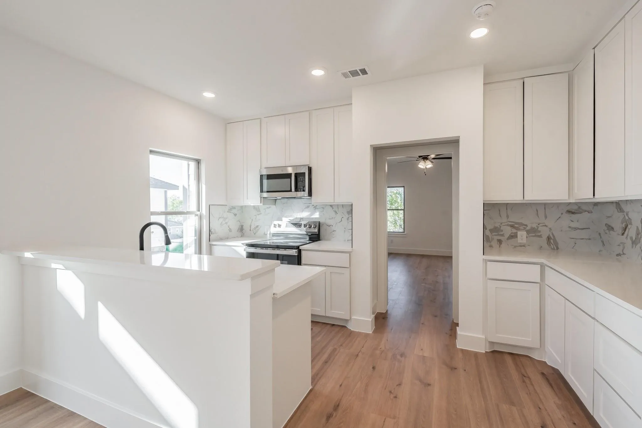 Bright kitchen featuring white cabinetry, light countertops, stainless steel appliances, wood-finish flooring, and recessed lighting