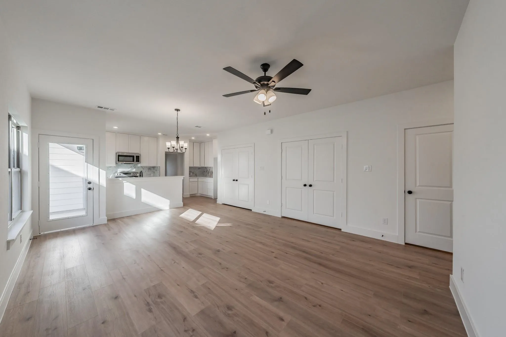 Open-concept living space with wood-finish flooring, a modern ceiling fan, and a kitchen featuring white cabinetry, stainless steel appliances, and a central island