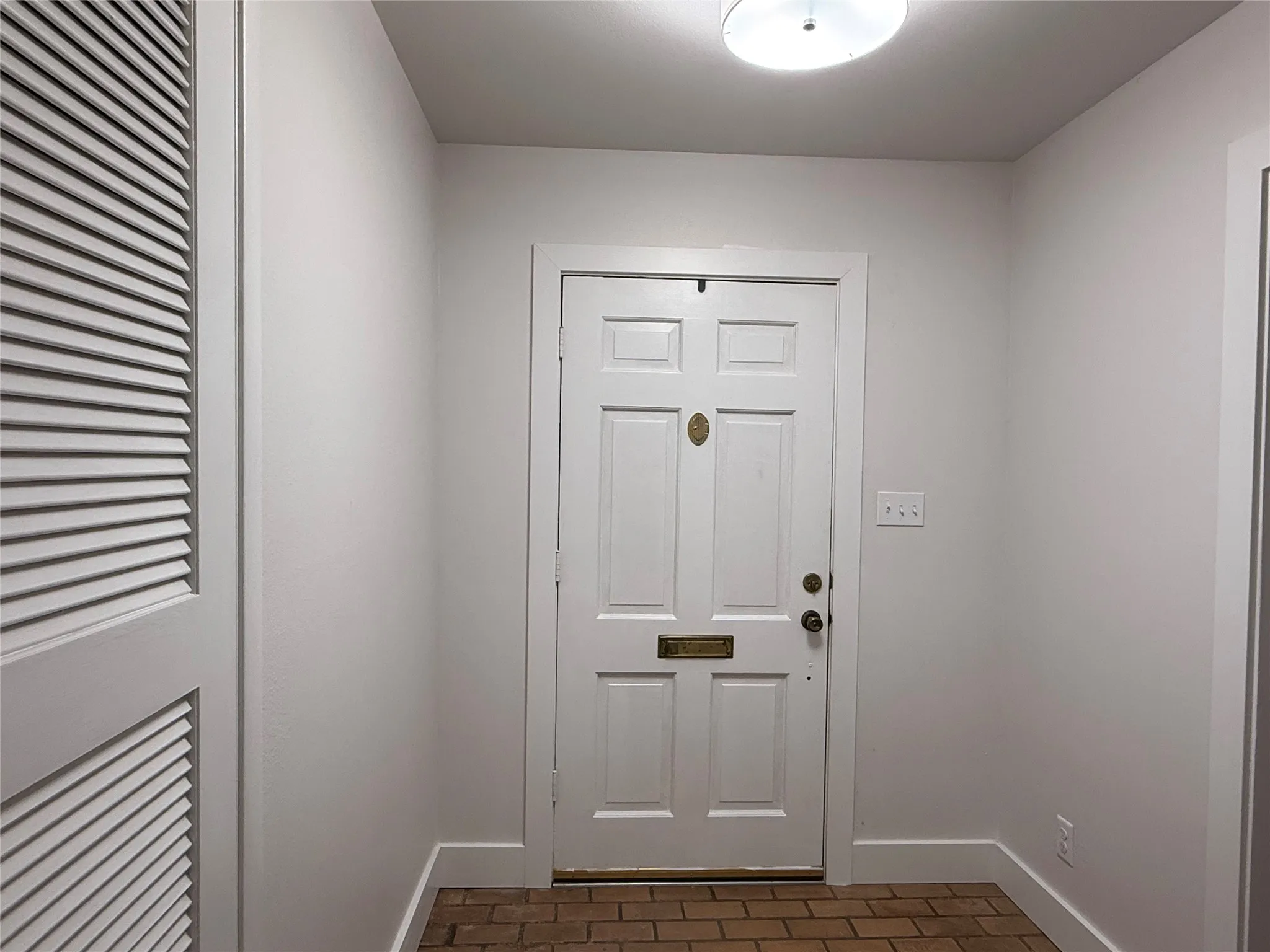 Entryway with brick-style flooring, a four-panel door, and a louvered bi-fold closet