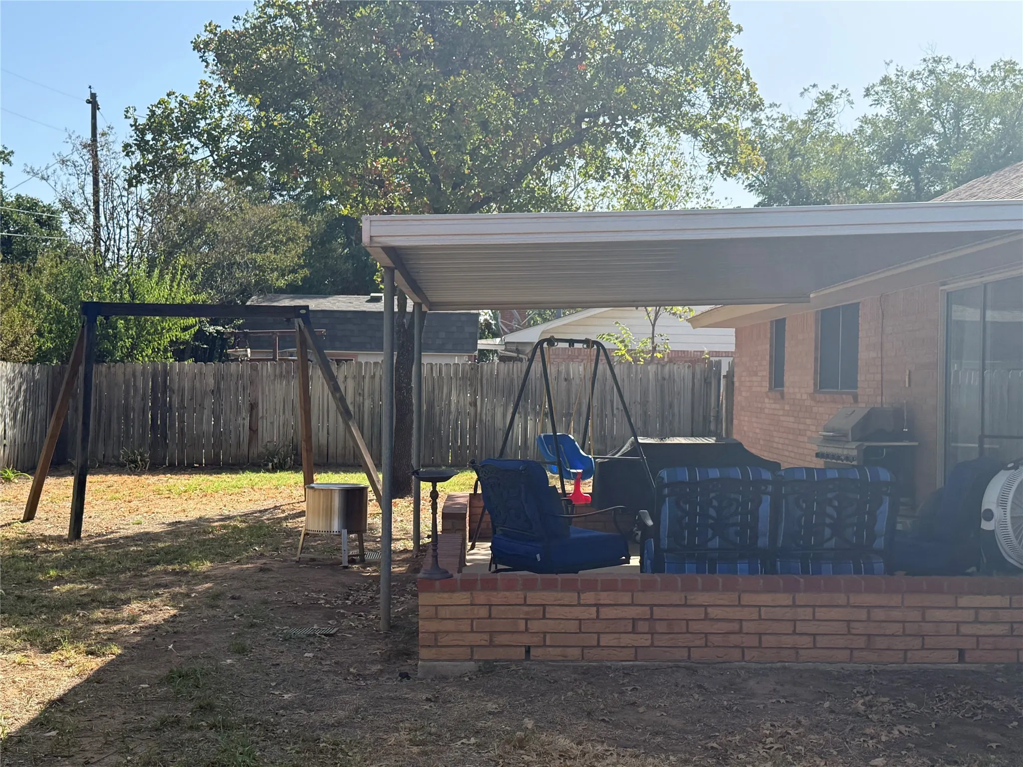 Expansive backyard with a full privacy fence, covered patio, and brick exterior