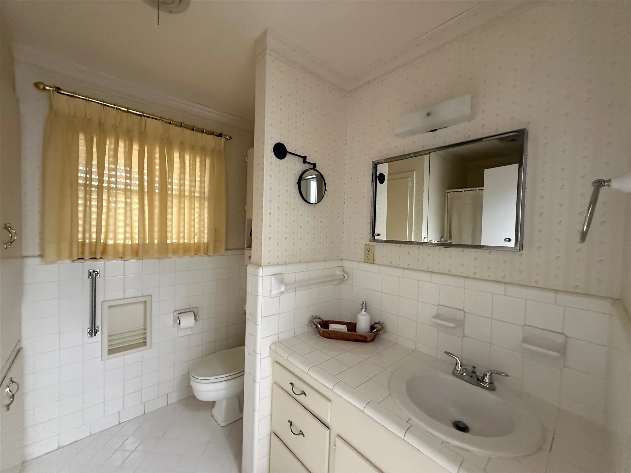 Vanity with an integrated sink and tiled countertop, framed mirror, wall-mounted light fixture, and tiled walls