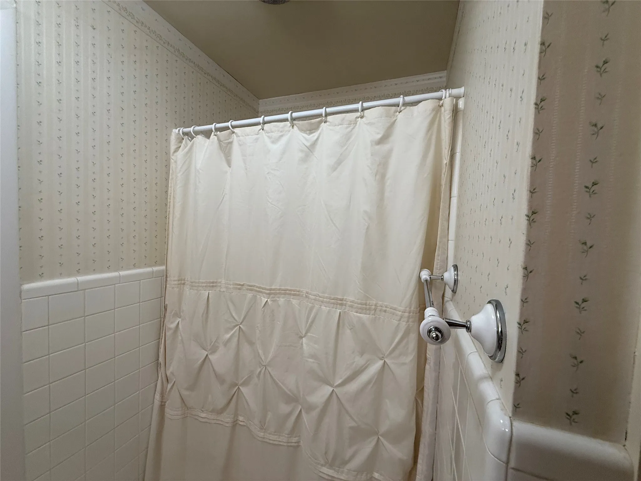White tiled shower surround with decorative wallpaper