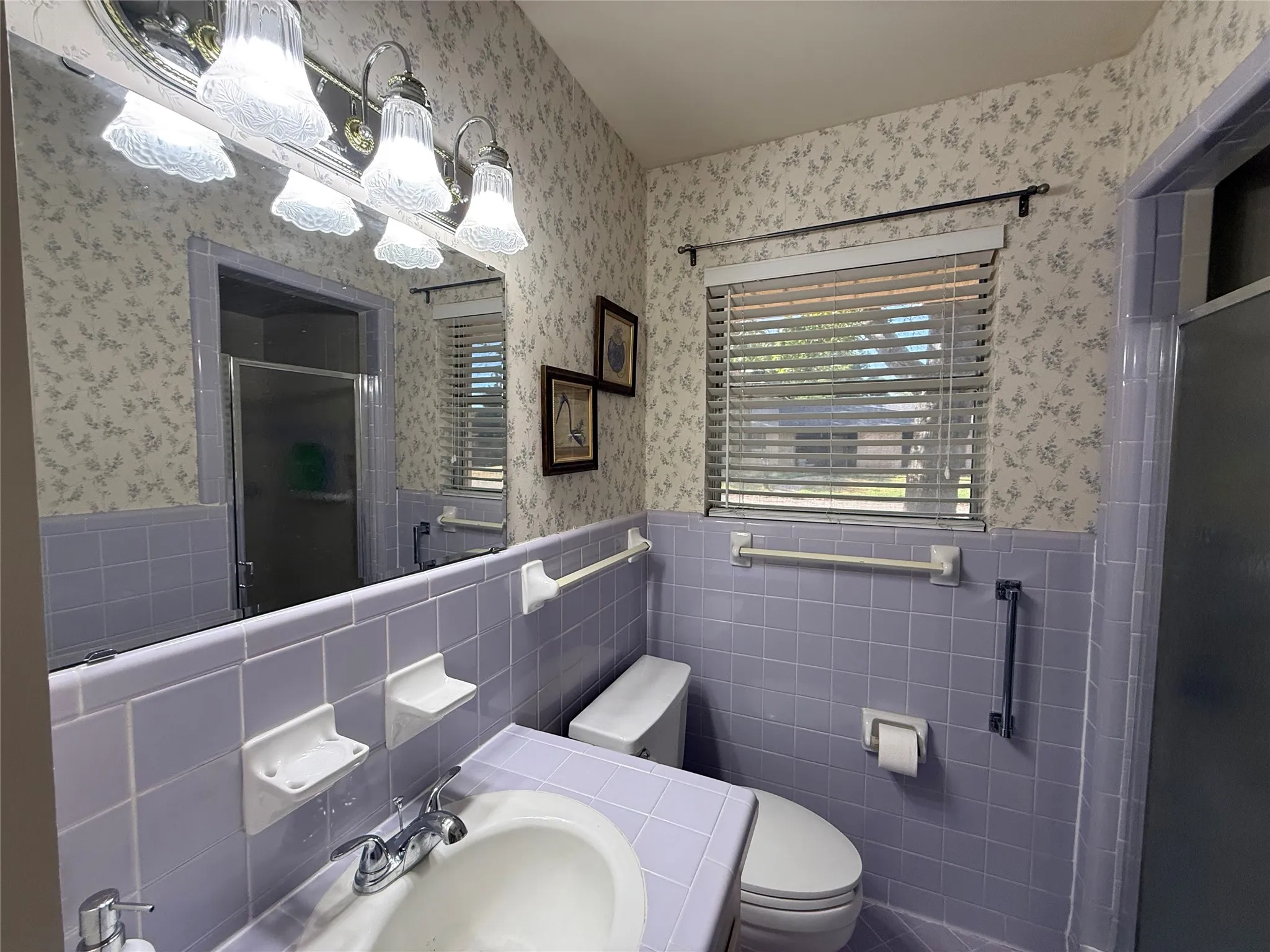Bathroom with a window featuring horizontal blinds, a vanity with an integrated sink, a wall-mounted mirror, and a toilet
