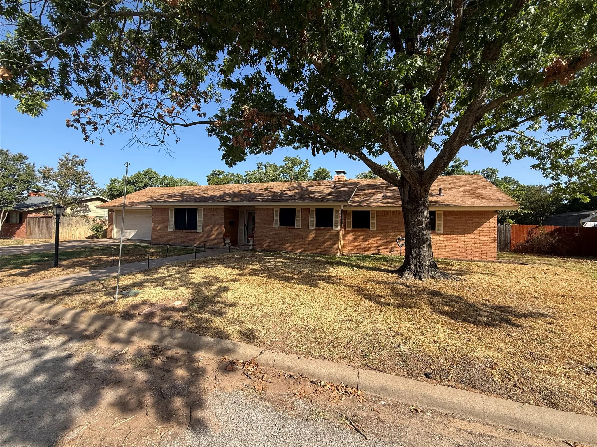 Brick exterior traditional home with a shingle roof, attached garage, and mature front yard tree