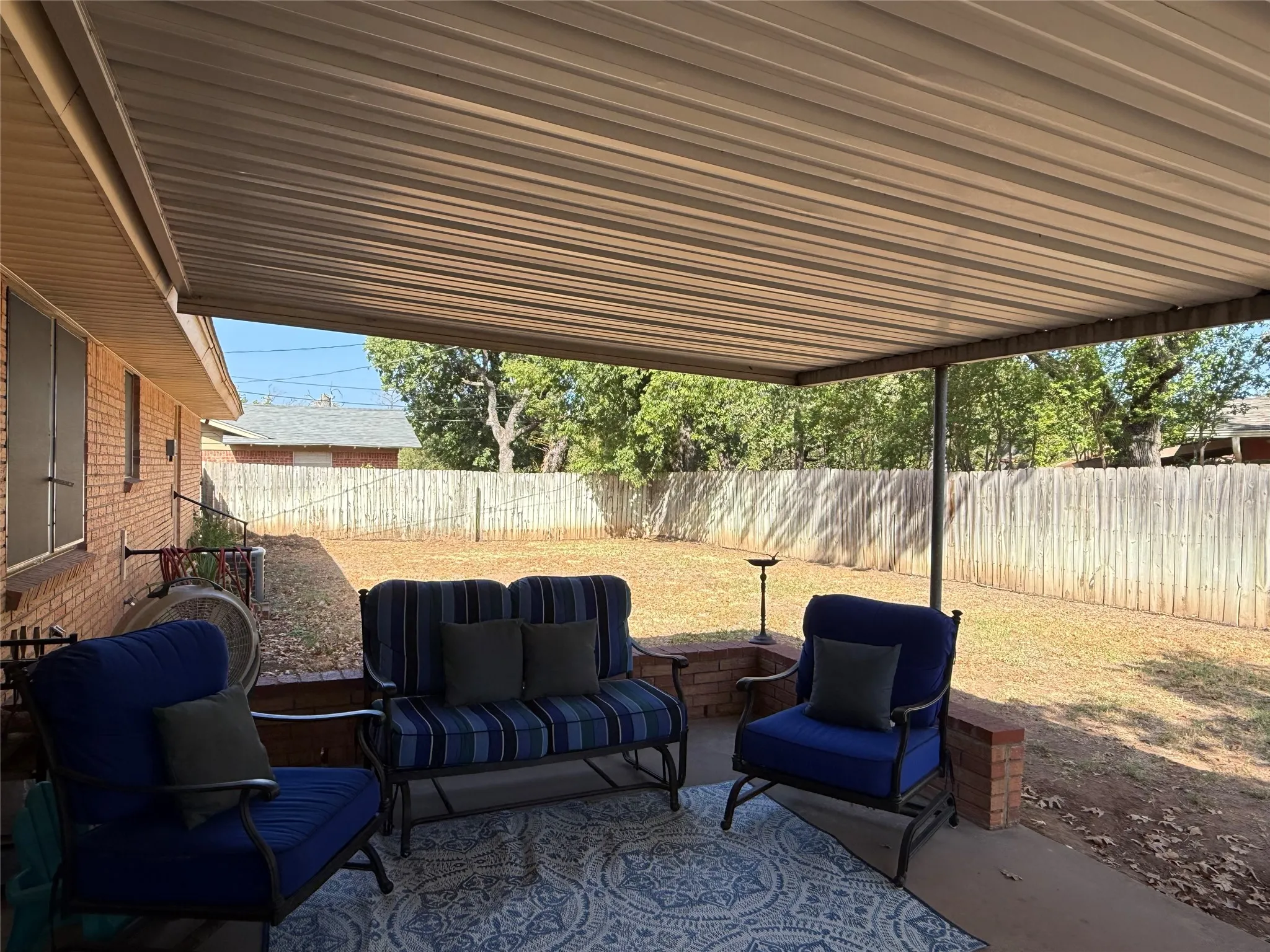 Covered patio featuring a solid roof, concrete slab, brick accents, and a wood privacy fence