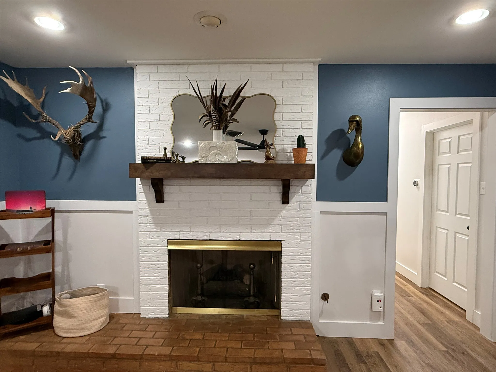 White brick fireplace with a wood mantel, brick hearth, and gold-toned fireplace insert