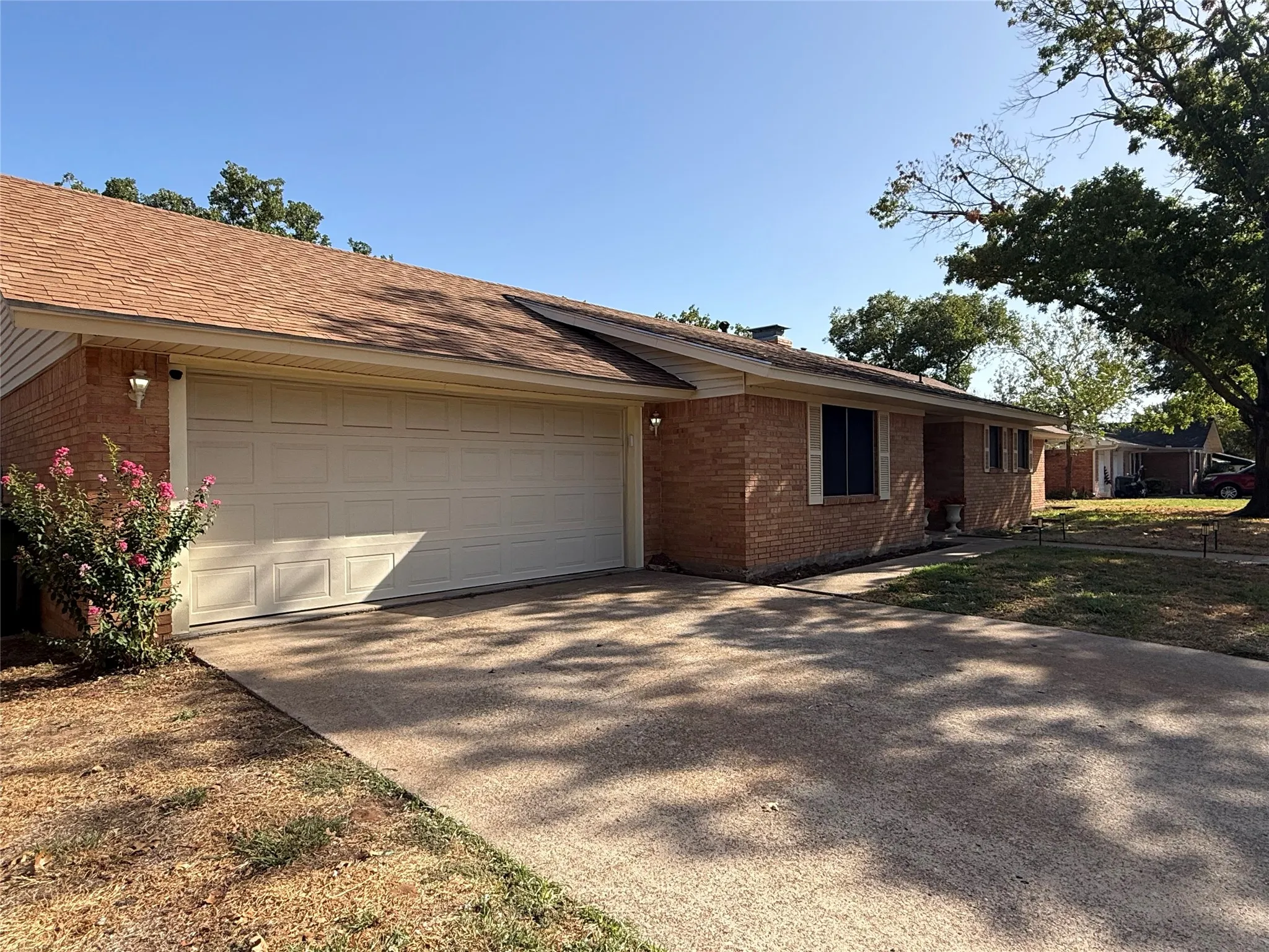 Brick exterior with a peaked roof, attached garage, and a concrete driveway