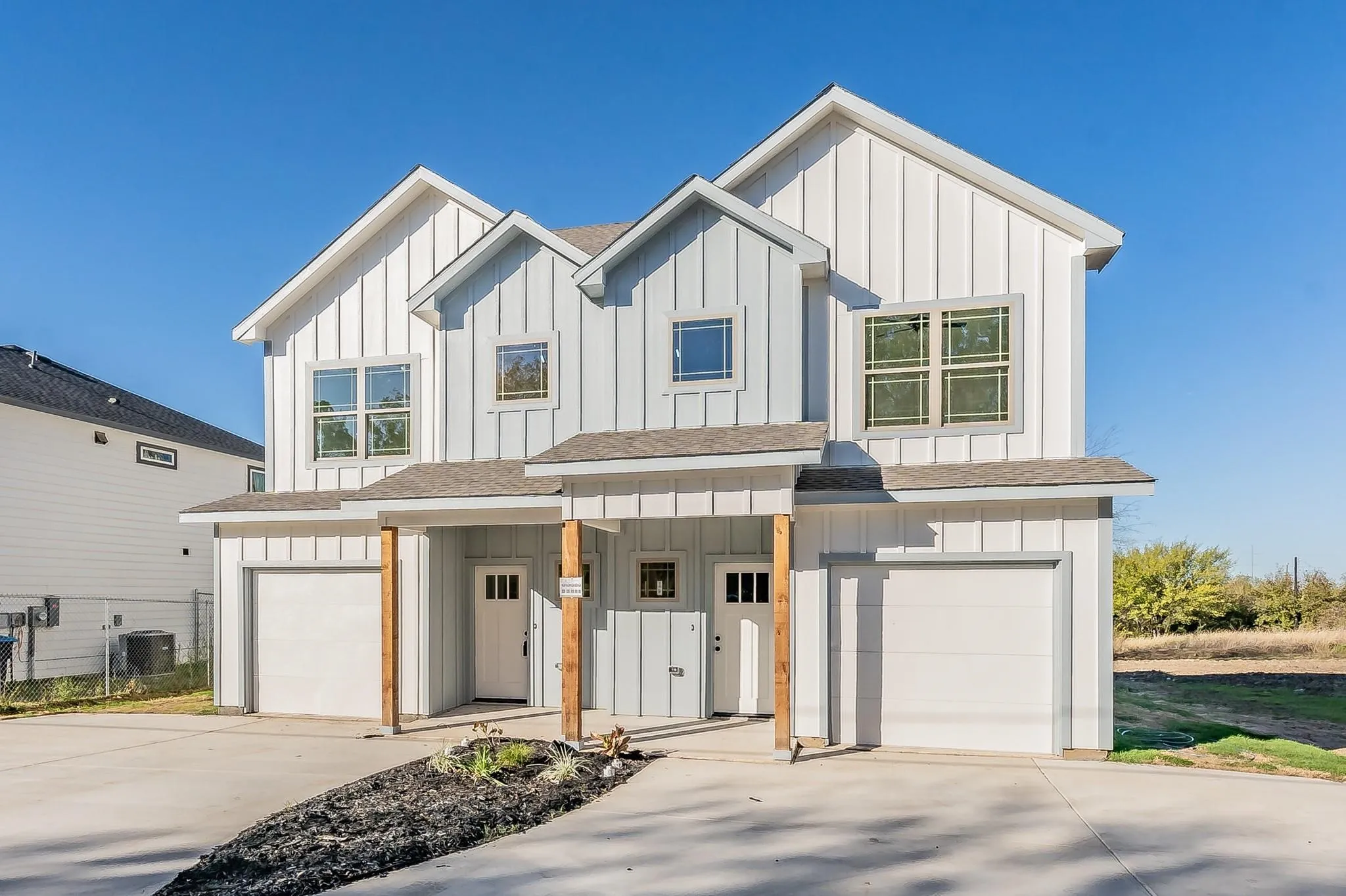 Duplex featuring modern vertical siding, individual garage access, distinct entryways with wood-toned support beams, and multiple windows