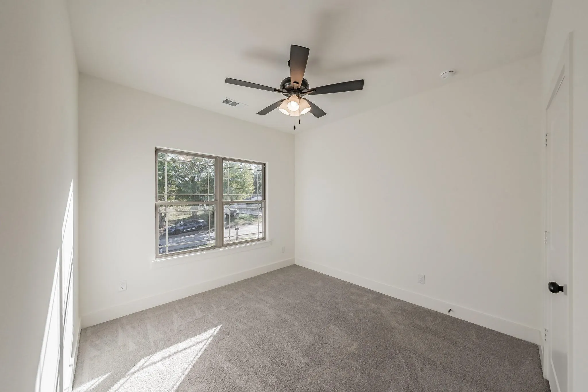 Vaulted ceiling with an attached ceiling fan, large window with grid panes, neutral-toned carpet, and a solid interior door with dark hardware