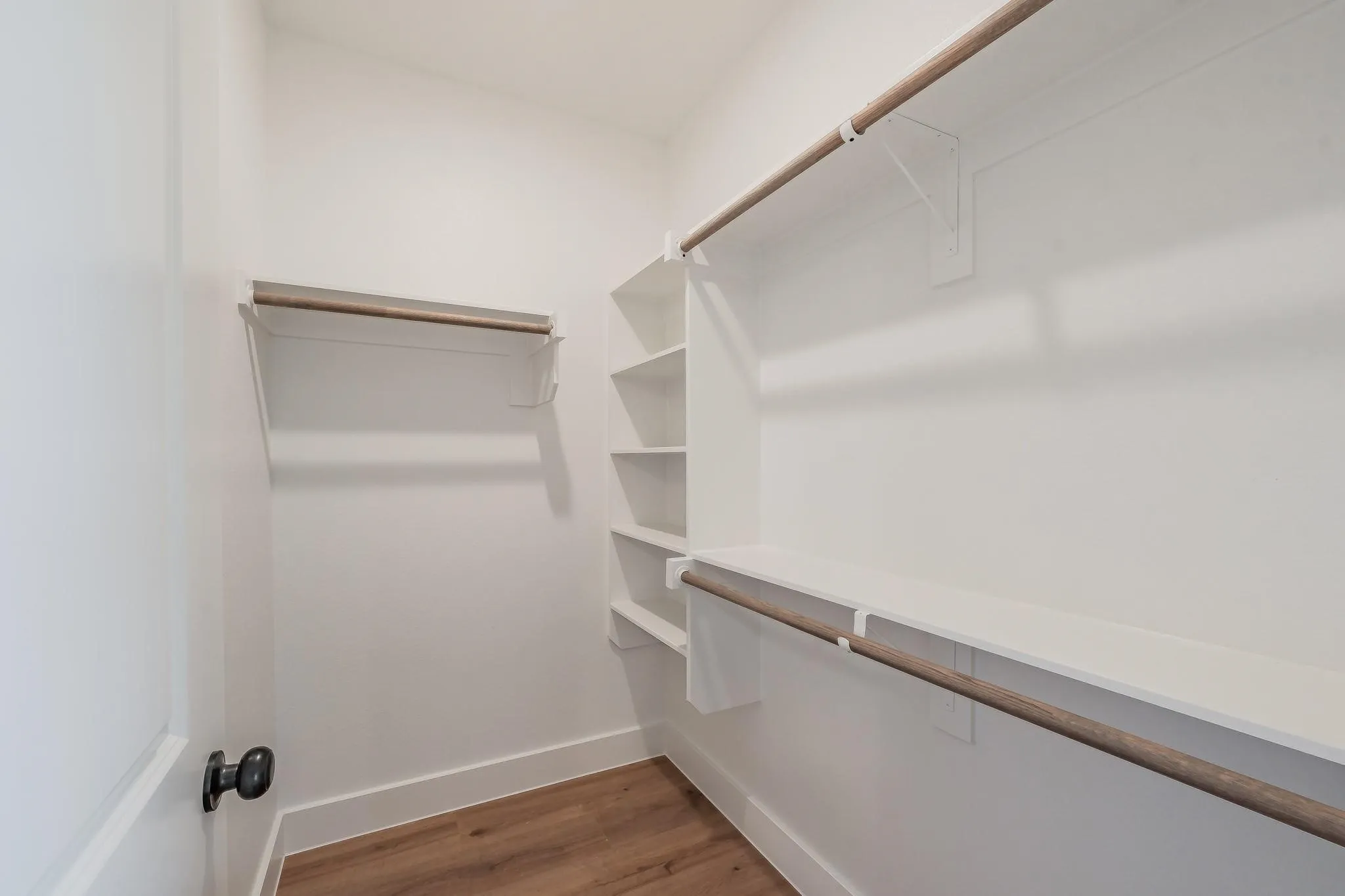 Integrated shelving system with multiple storage rods, white walls, and wood-finish flooring