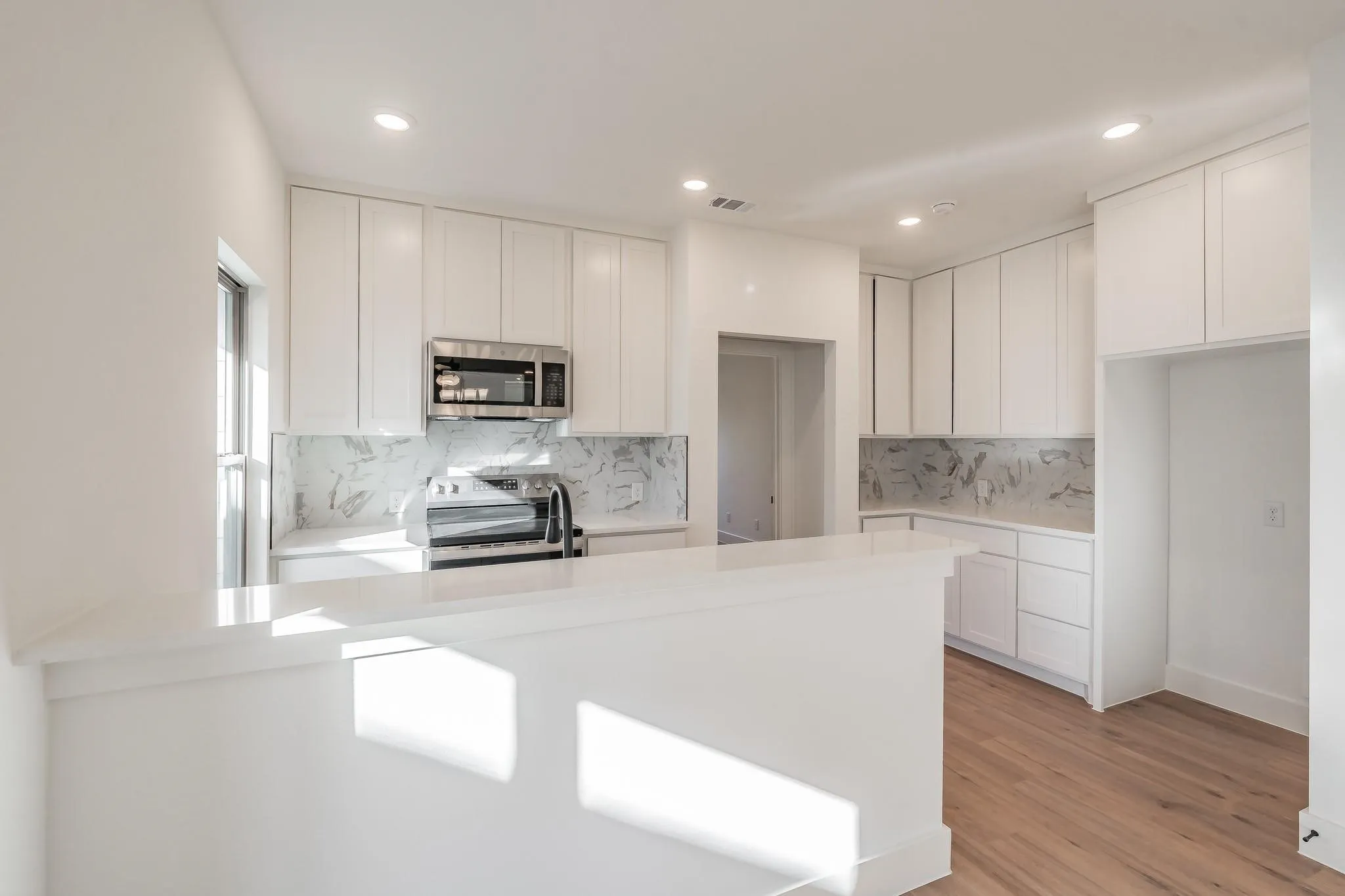 Contemporary kitchen featuring white cabinetry, a dedicated microwave, a stainless steel range, light-toned wood-finish flooring, and recessed lighting