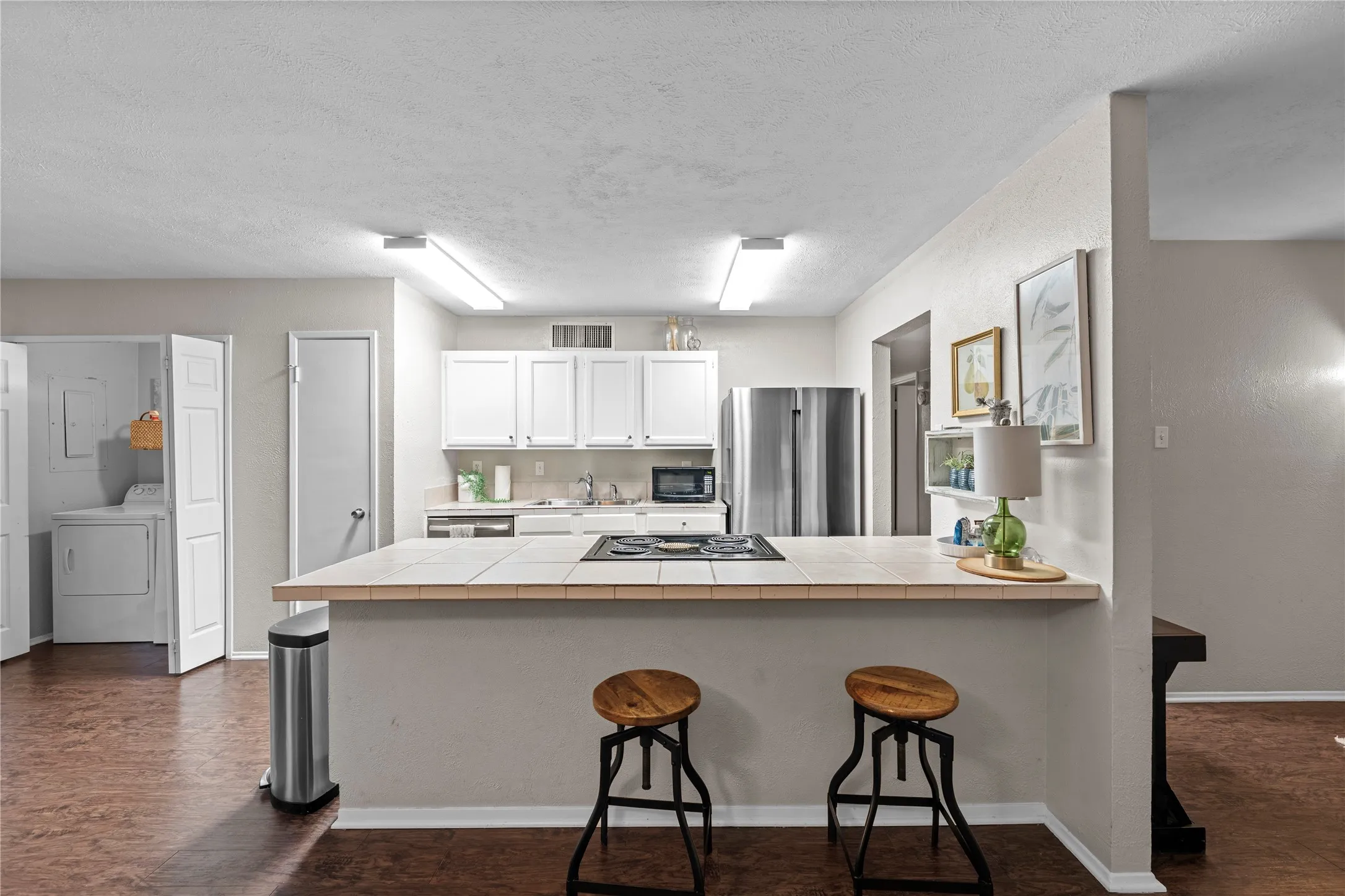Kitchen featuring white cabinetry, tile countertop island with cooktop, stainless steel refrigerator, and wood-finish flooring