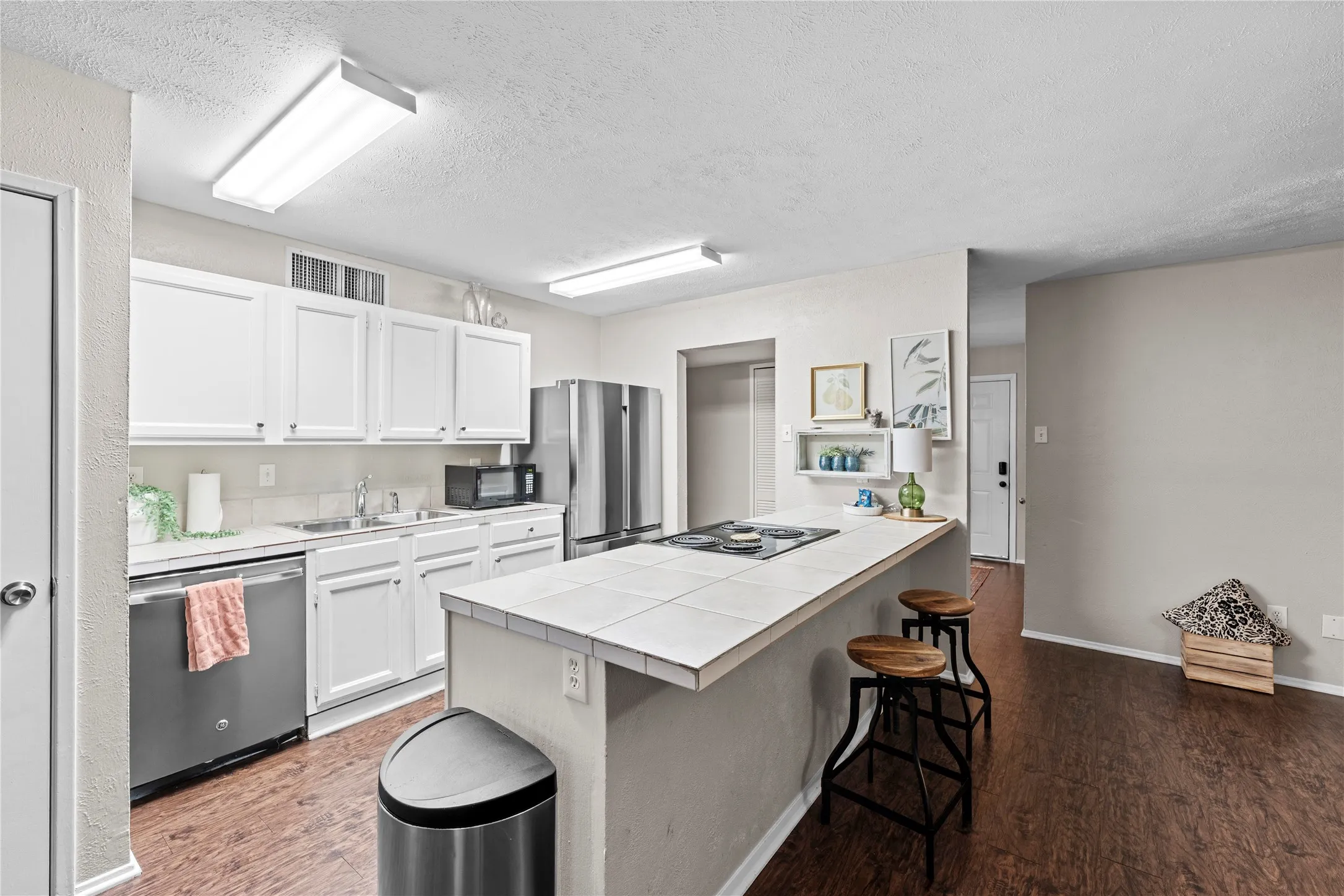 Kitchen featuring white cabinetry, stainless steel appliances, a tiled island with an integrated cooktop, wood-finish flooring, and recessed lighting